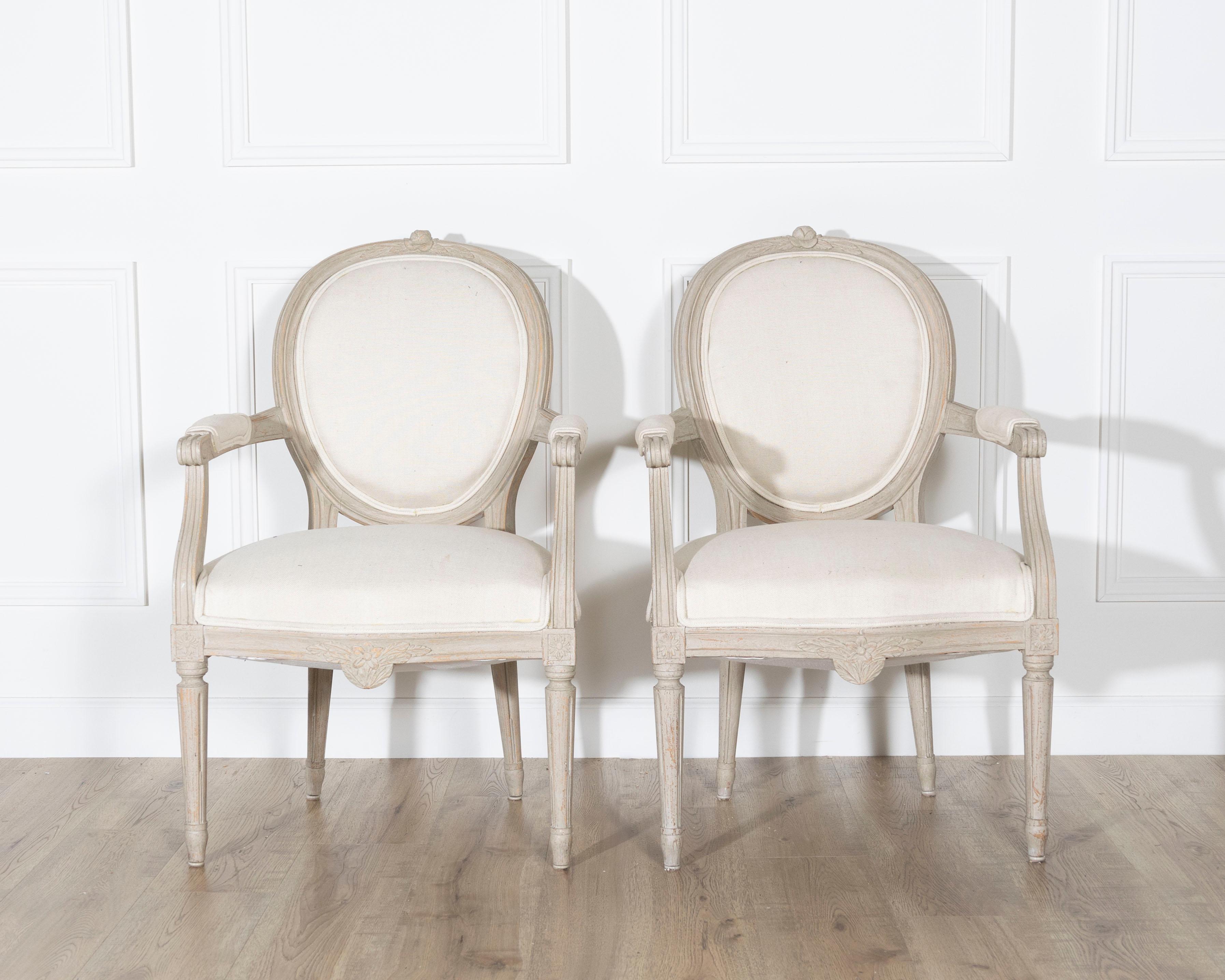 A refined pair of Gustavian style armchairs from Sweden, dating to the early 20th century and crafted in the neoclassical tradition. Each chair features an oval backrest with molded frames and subtle floral crest carvings, exuding the light,