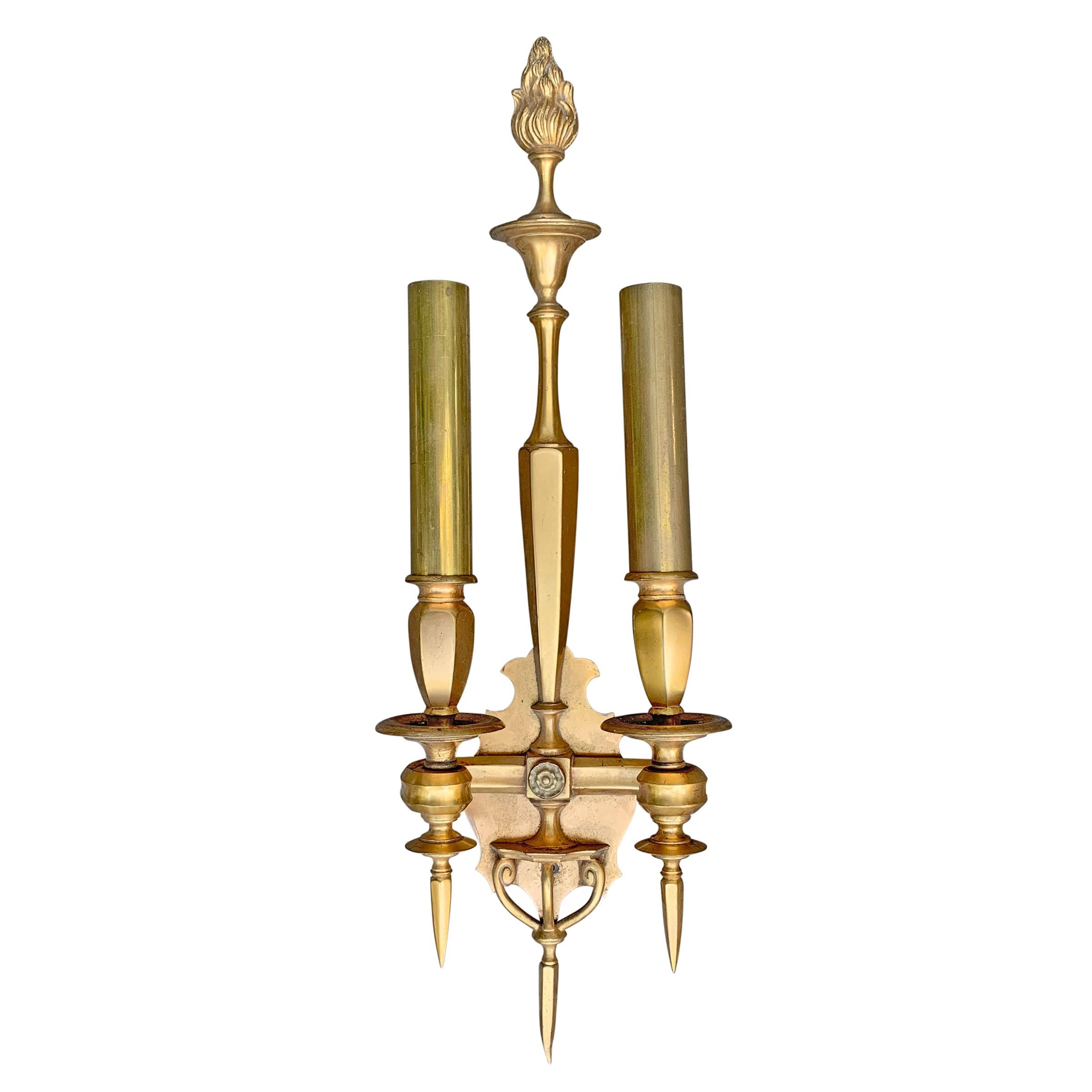 A pair of uber chic early 20th century Swedish bronze and brass two-arm sconces, each with two scrolled arm holding vase-form candle cups, and a long slender backplate topped with a neoclassical style flame. Sconces are electrified.