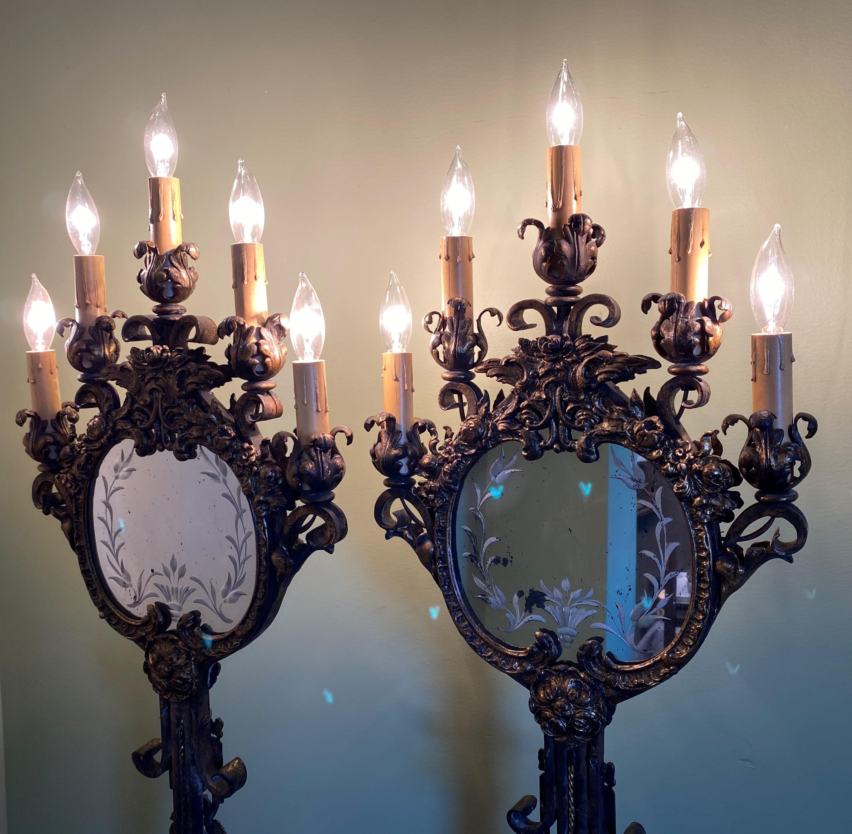 A finely crafted pair of gilt wrought iron electrified five light torchieres with etched mirrors and beautifully appointed foliate and scrolled metalwork, on shaped variegated marble bases, dating to the early 20th century. This heavy pair of