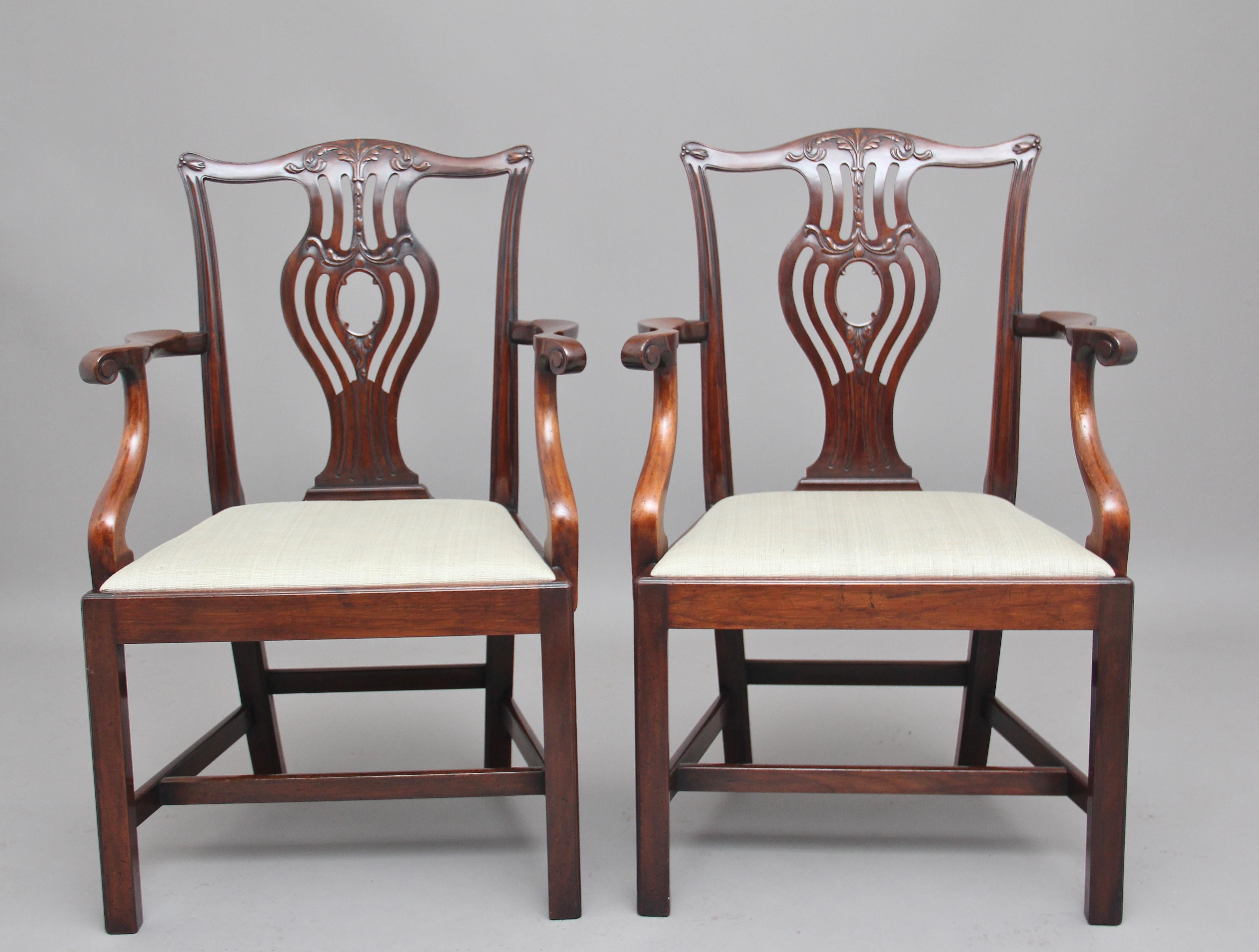 A pair of early 20th century mahogany armchairs in the Chippendale style, the slender curved supports with scroll decoration on the front of the arms, with a pierced and carved back splat at the centre, with a grey fabric upholstered drop in seat,