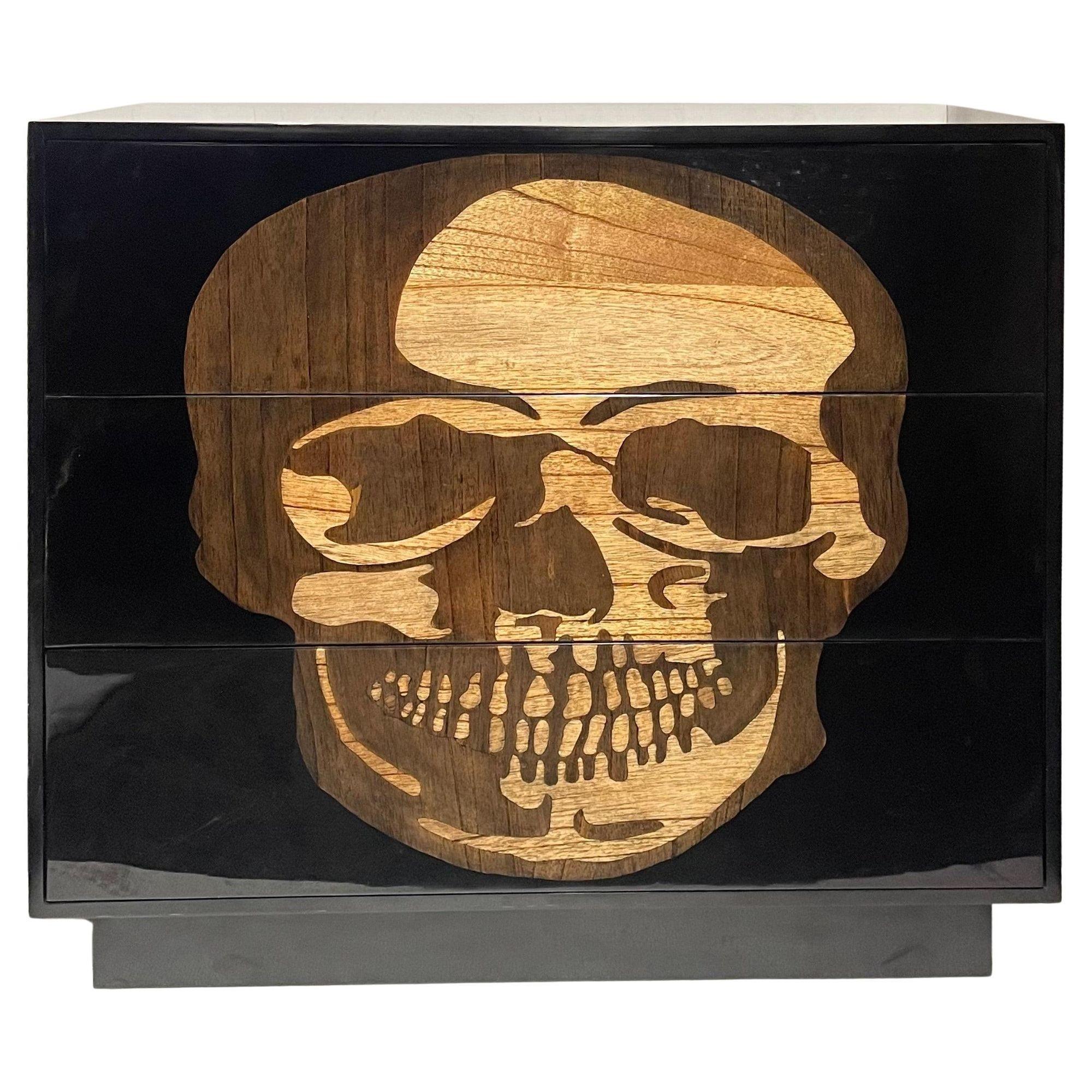 This striking pair of early 21st-century black commodes features an intricate skull design, inlaid in wood and finished with a high-gloss resin that accentuates the bold craftsmanship. These pieces blend contemporary design with edgy artistry,