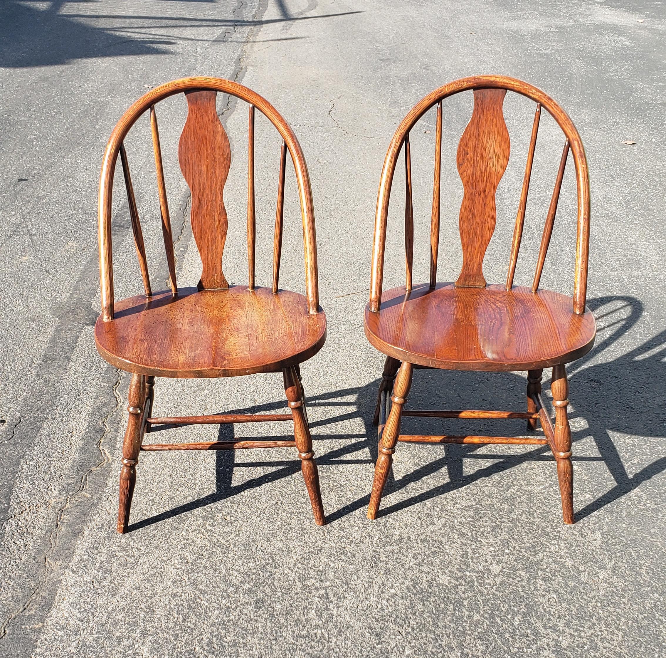 A pair of early American style wide red oak Windsor side chairs in good vintage condition. Structurally sound pair of chairs. Measure 19.5