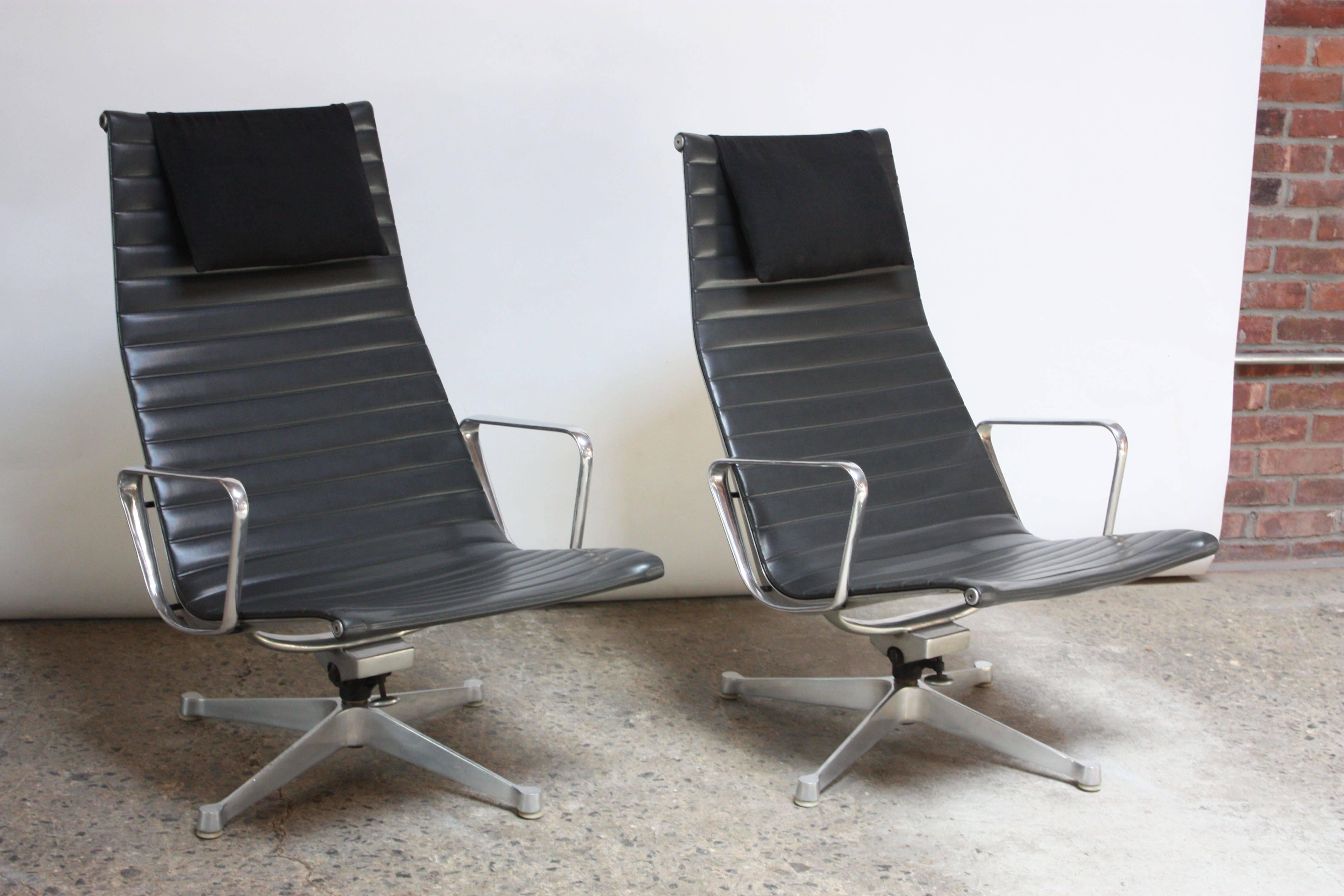 Early pair of high-back lounge chairs with swivel / tilt function designed by Charles and Ray Eames and manufactured by Herman Miller as part of the Aluminum Group collection. Composed of black channelled vinyl seats with headrests on four-point