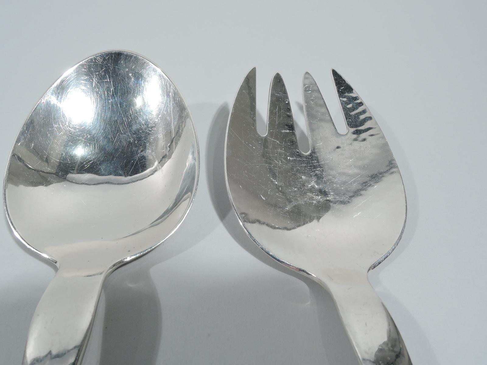 Pair of early sterling silver salad servers. Made by Georg Jensen in Copenhagen. This pair comprises spoon with wide oval bowl and fork with wide and curved 4-tined shank. Each has open knotwork-style scrolled terminal in form of leafing branch. A