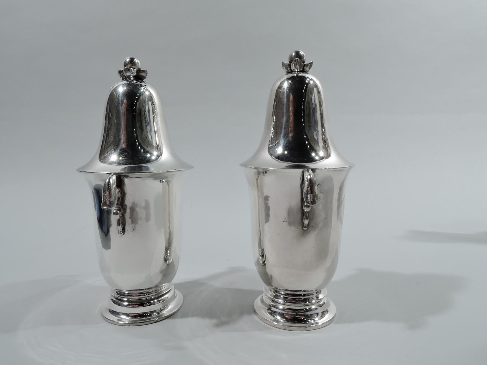 Pair of Art Nouveau sterling silver salt and pepper shakers. Made by Georg Jensen in Copenhagen, ca 1915. Each: Tall body with curved bottom and round and stepped foot. Small leaf-capped scroll side handles. Top domed with stylized flower-head