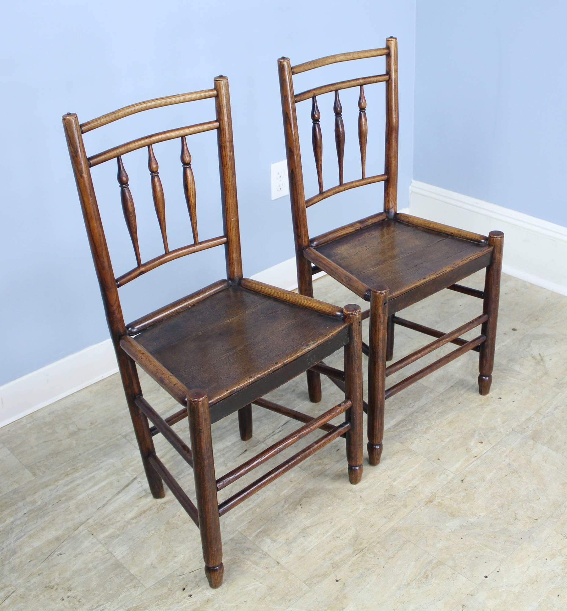 A charming pair of early oak side chairs with delicate spindle backs and double supports. Rich dark oak with lovely patina and articulated edges at the seat, which measures 17 inches high. These chairs are delicate and more decorative than for