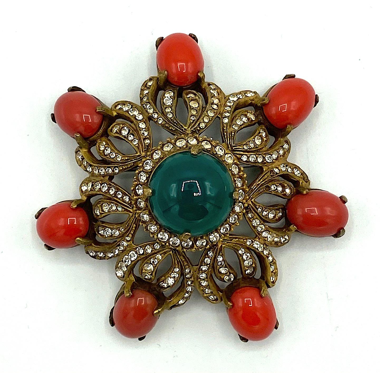 A very rare pair of pre 1973 medallion brooches by Kenneth Jay Lane. They have an openwork and domed design that features a large top emerald green glass cabochon, rhinestone accents and seven oval glass coral color cabochons. Each brooch has a hook