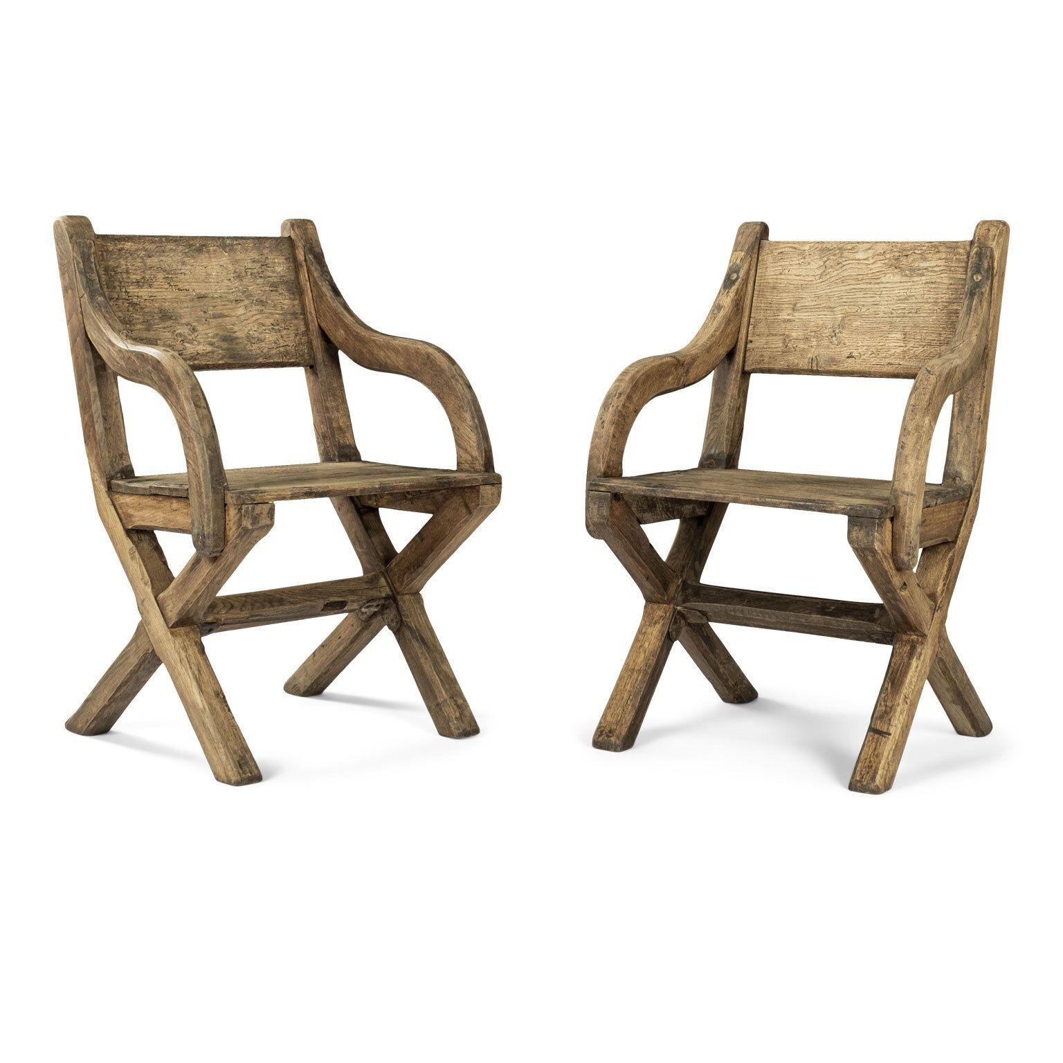 Pair of early oak x-frame armchairs designed in a Glastonbury type style. Chairs feature rectangular backs, curved arm supports and solid seats. X-frame sides united by stretcher reinforced by original iron strapping. Hand-hewn from English oak