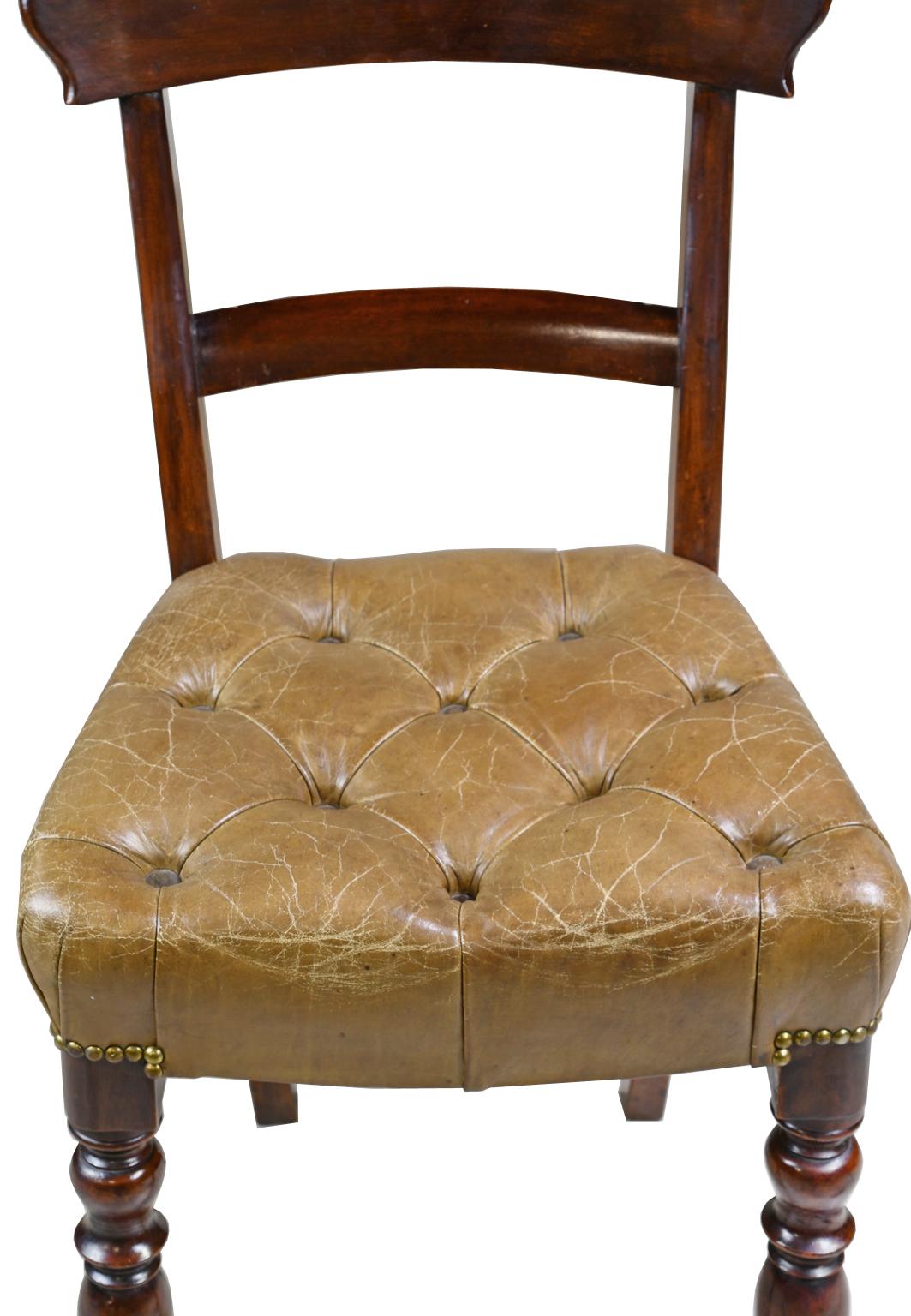 A pair of early Victorian side chairs in mahogany with curved top rail, and raised on turned front legs and saber back legs. Seat is upholstered in a tufted, beige/camel-colored leather with brass nailheads, England, circa 1840. 

Measures: 18