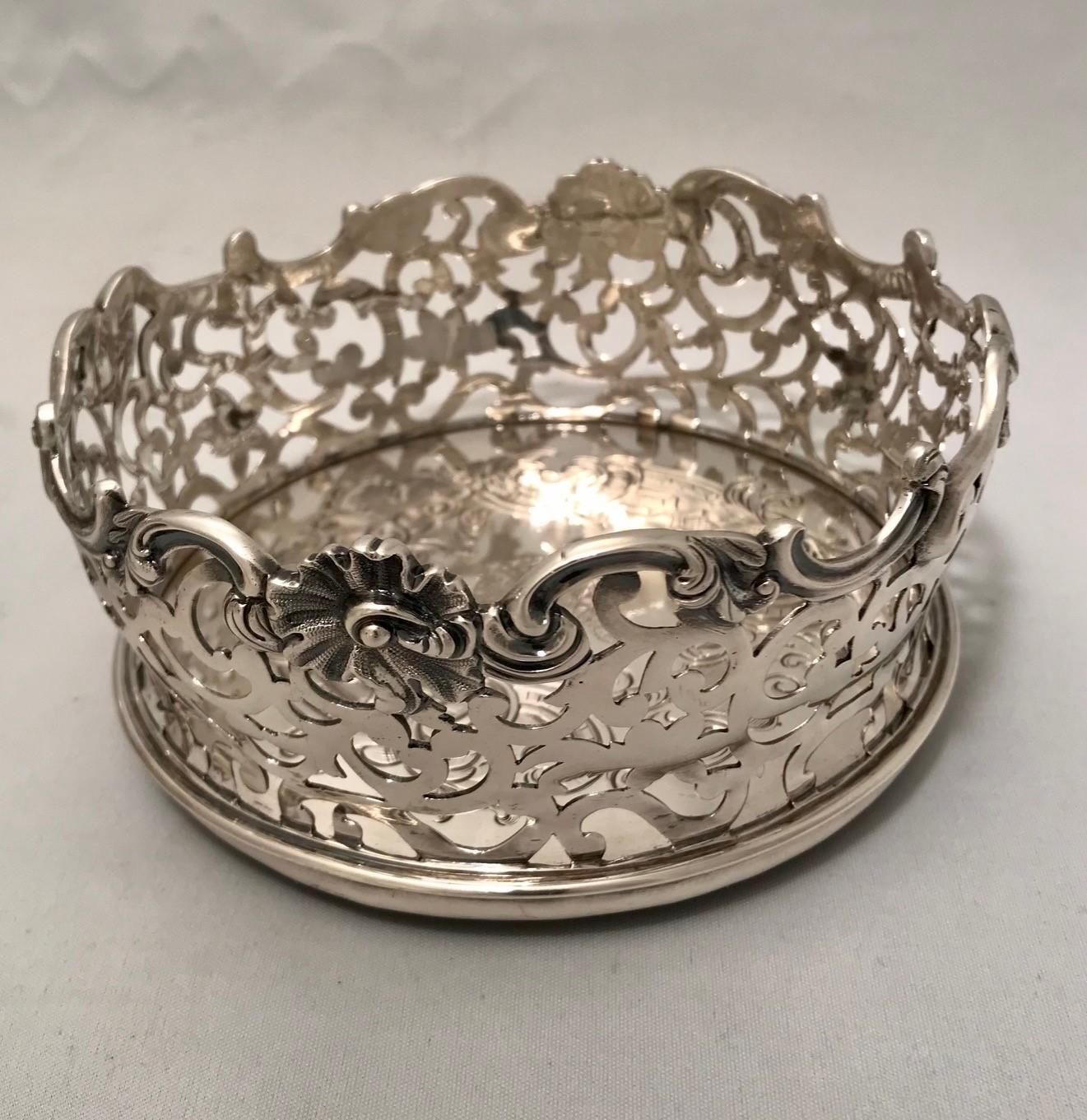 This is a magnificent pair of Victorian silver wine bottle coasters, pierced and with undulating shell and scroll mounted rims. Usually the wooden base is left au naturel but in this case it is also silver and engraved with the Order of the Bath and