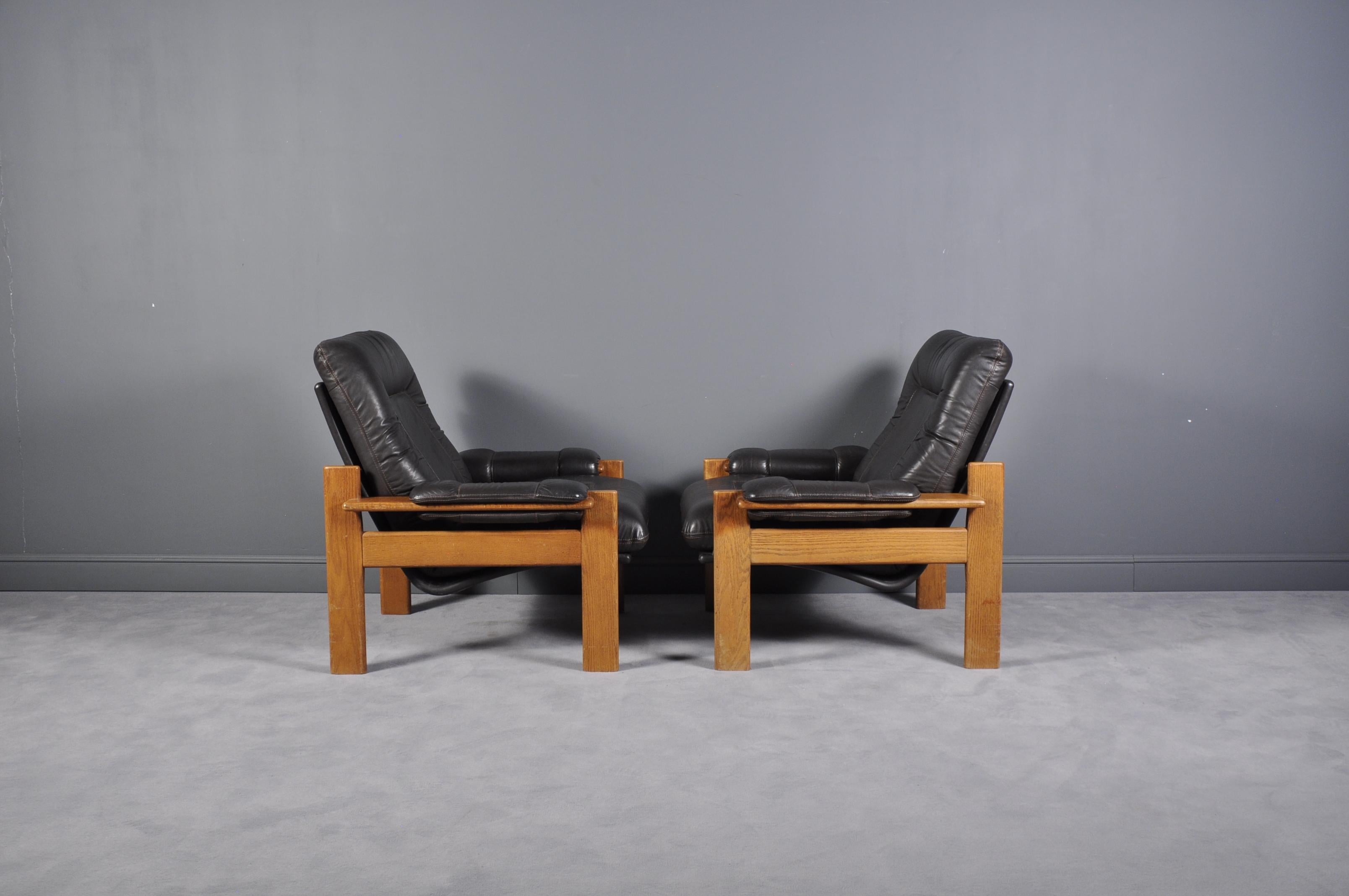 This set of easy chairs features a teak frame with a black leather seat and back. The chairs have a sturdy frame showing refined craftsmanship, holding a comfortable leather shell. The seat and back are well proportioned and provide excellent back