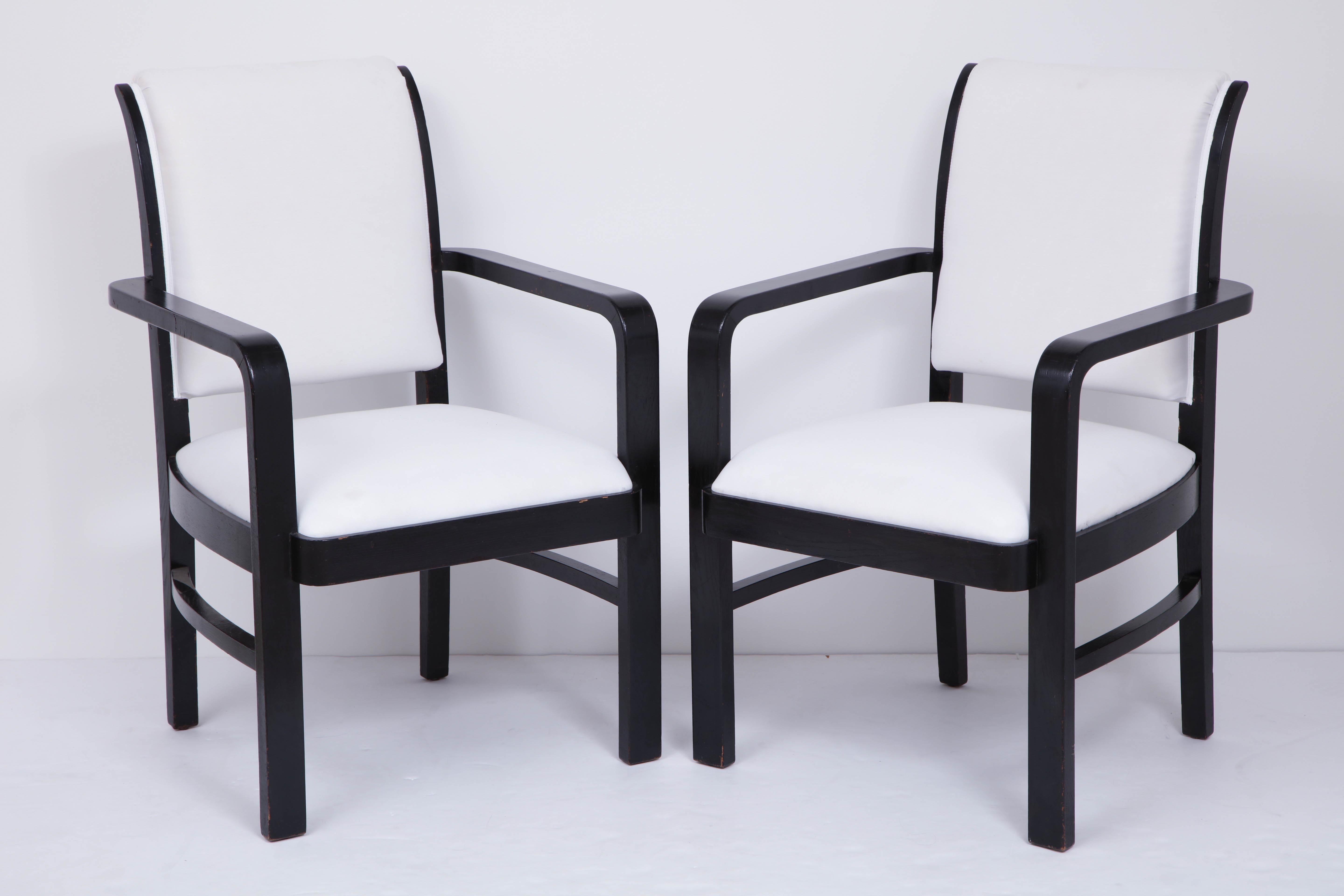 Pair of ebonized armchairs, square back and seats. Open arms continuing to legs joined by stretcher.