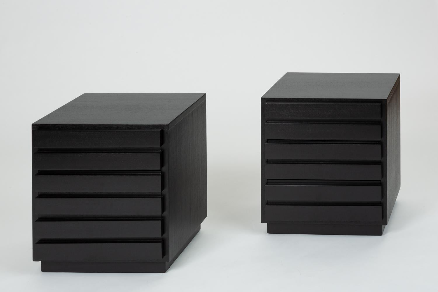 A pair of nightstands from Virginia-based manufacturer, American of Martinsville from the 1950s. The boxy storage pieces sit on a recessed plinth base with three two-panel drawers spaced evenly down the front. Redone with an ebonized finished, the