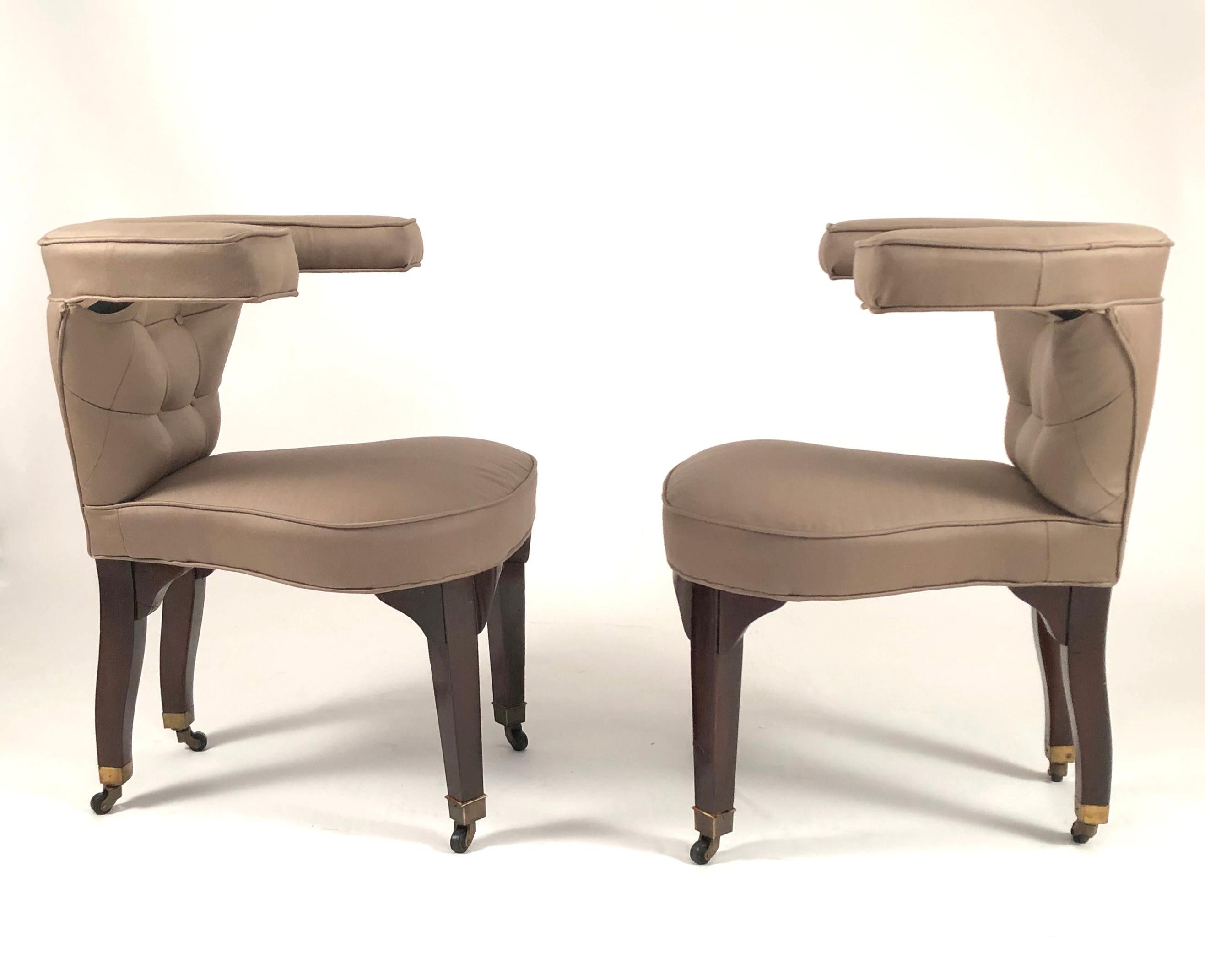 A pair of Edward Wormley designed cock fighting chairs made by Dunbar, newly upholstered in a khaki colored heavy weight twill, with button tufted backs and mahogany legs with brass caps and casters. This form is after a George III library chair,