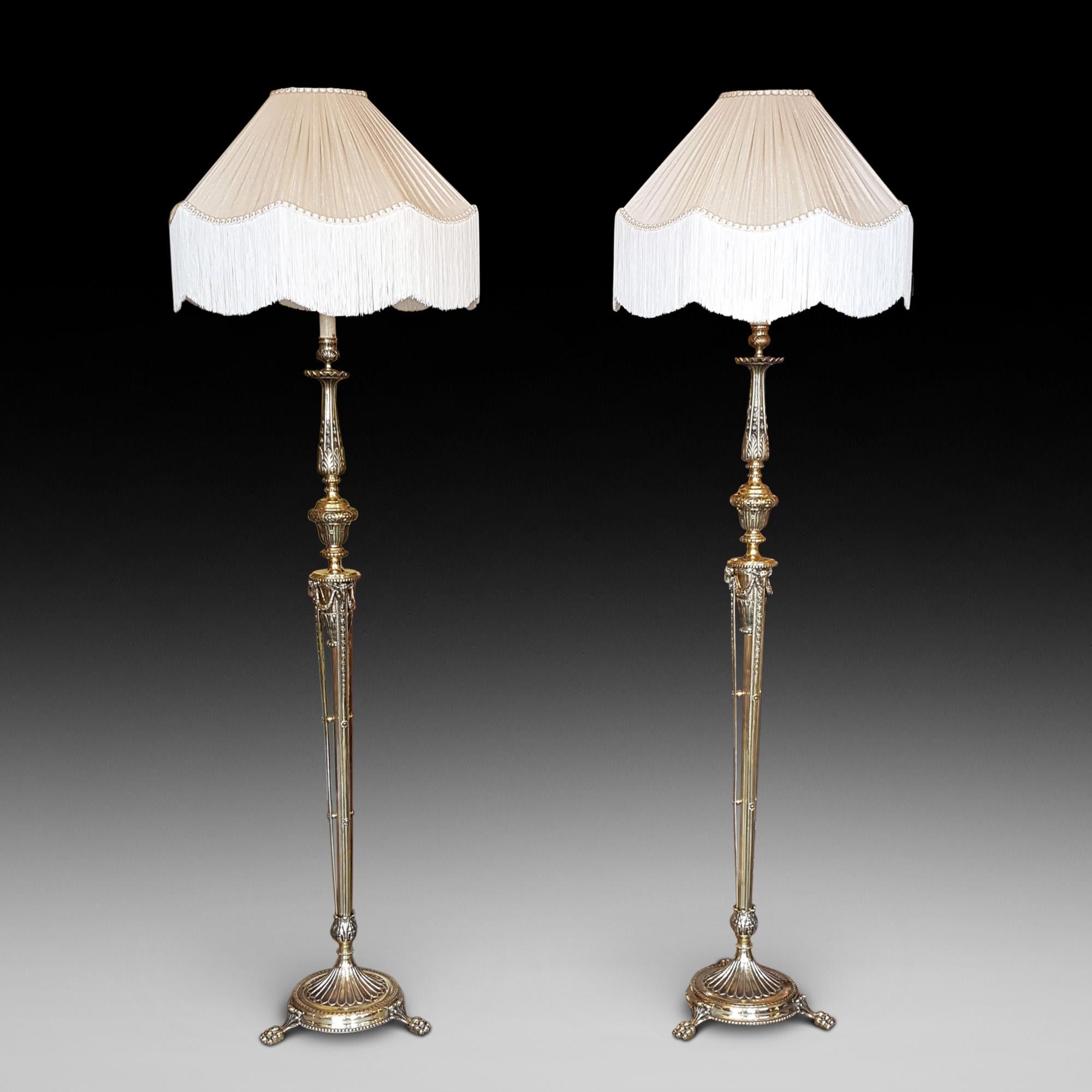 Pair of Edwardian Adam style brass lamp standards, each with bellflower and stiff leaf decoration and with rams heads to each vase support, raised on a circular base with paw feet, the lampshade(s) are newly handmade silks by the same maker as