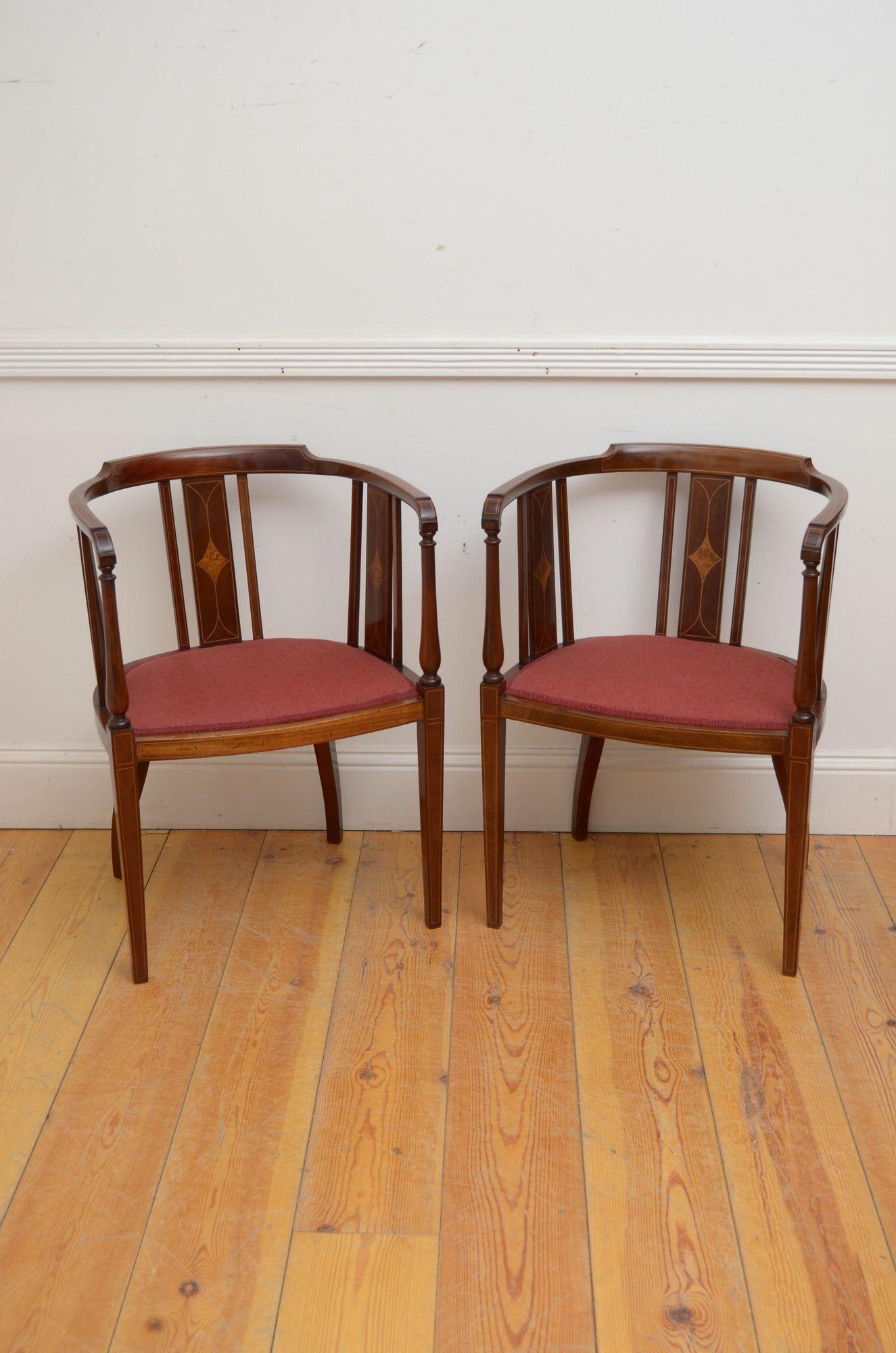 Sn5422 Pair of Edwardian tub chairs, each chair having shaped and inlaid top rail supported on inlaid uprights, open string inlaid arms and generous seat, all standing on slender, string inlaid legs. This pair of antique side chairs is in home ready