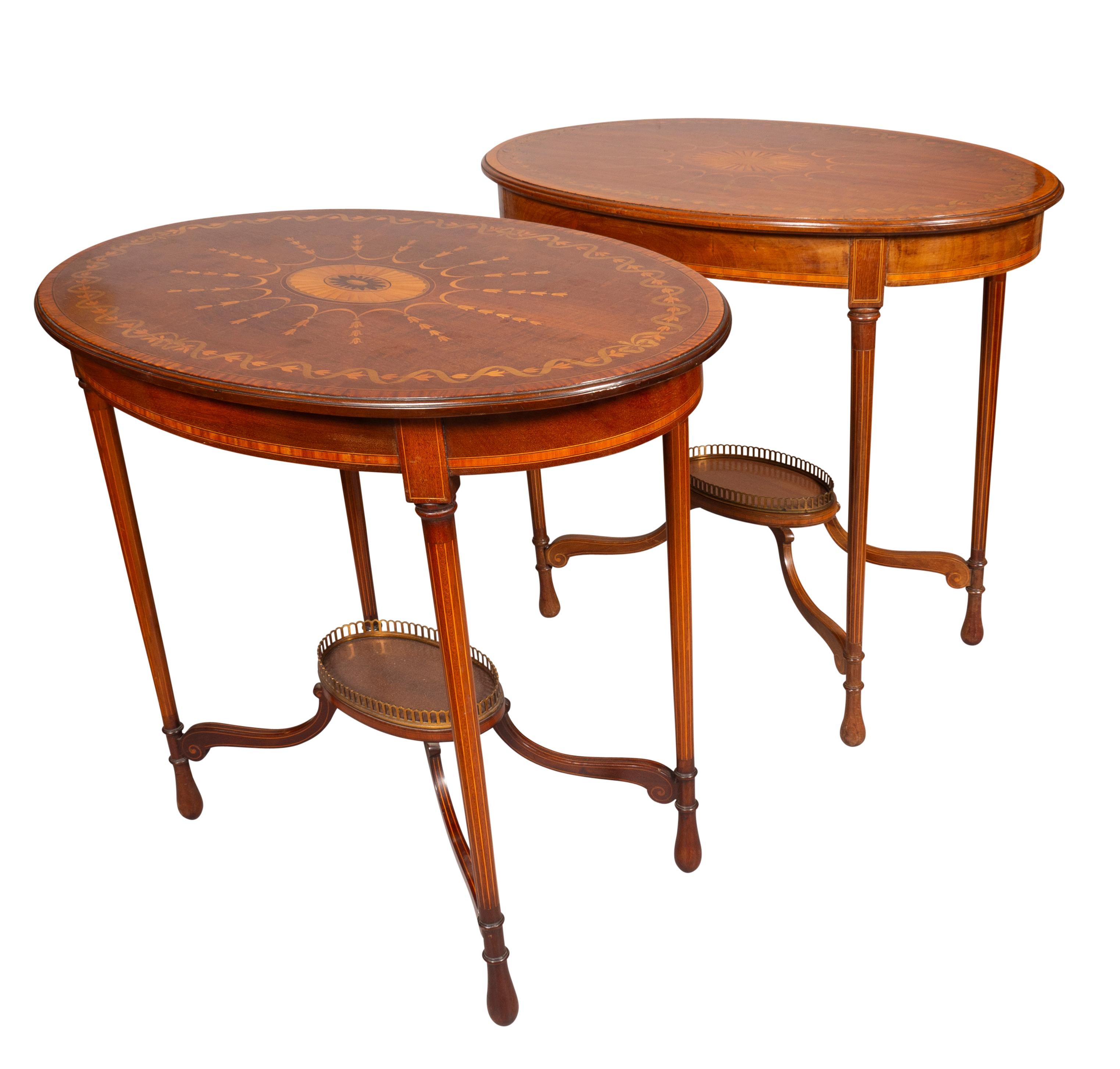 Each with oval tops with central paterae inlay with outer borders of different woods. Conforming apron raised on circular string inlaid tapered legs joined by a stretcher with central oval shelf with brass gallery.