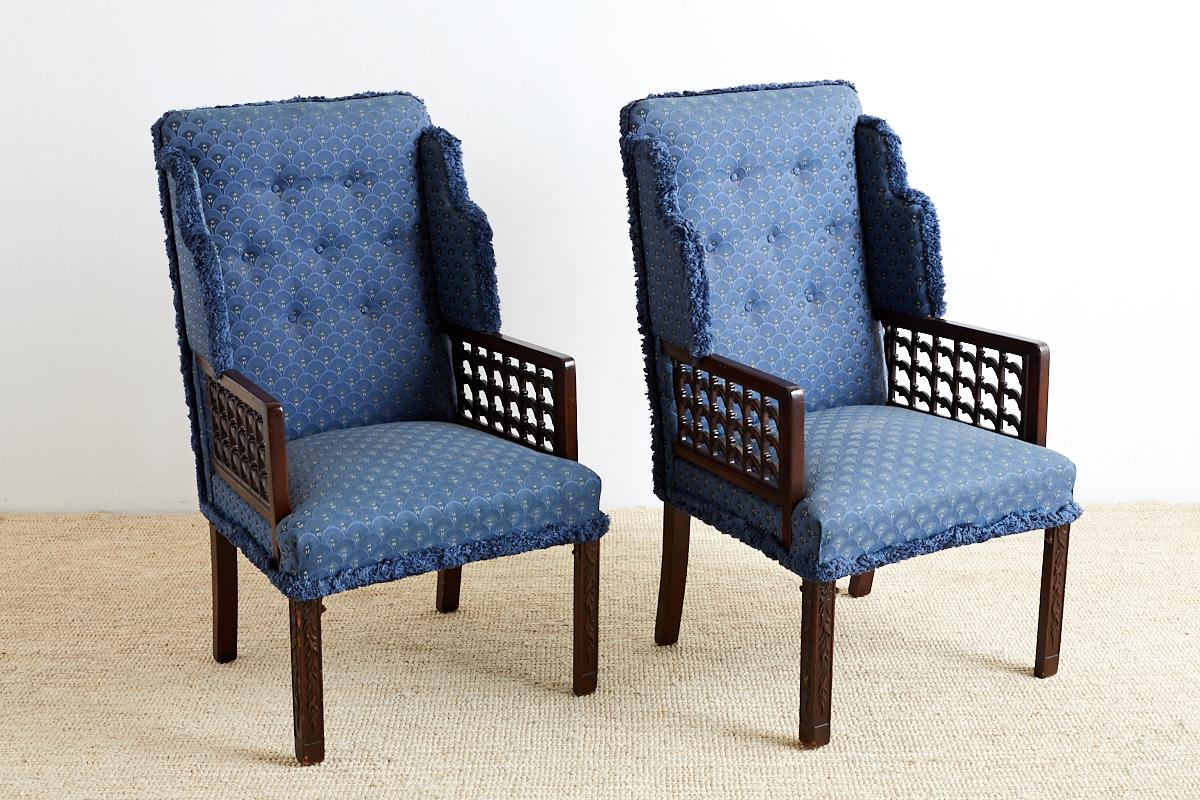 Interesting and unusual pair of Edwardian mahogany wing chairs featuring an open fretwork pattern of carved leaves on the arms. The armchairs have flat padded wings and are supported by square legs with decorative foliate motifs carved down the