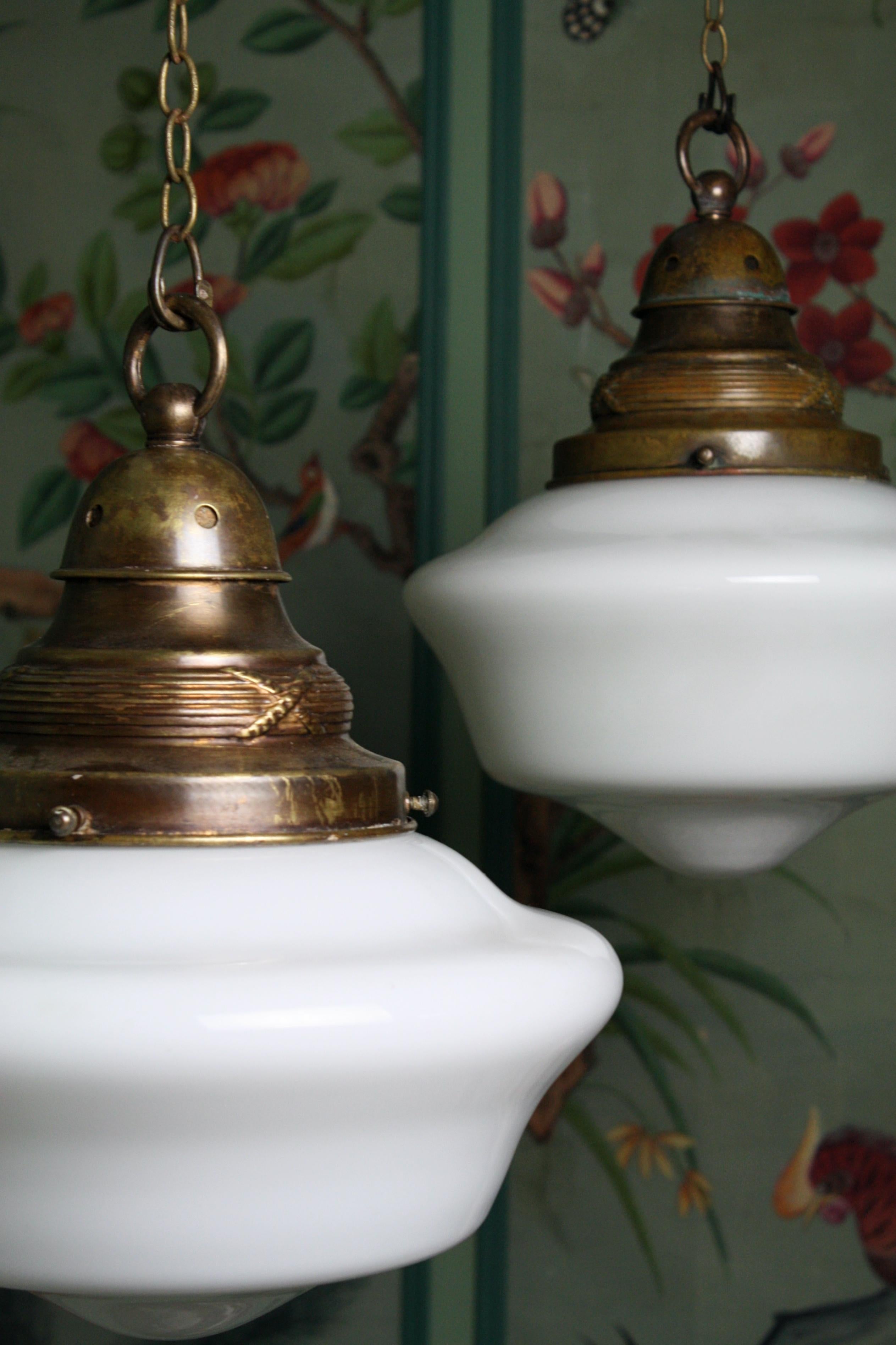 Pair of hand blown opaline glass pendants, with original heavy gauge brass galleries.

Each light has its original brass chain and ceiling rose, and comes with a length of three core silk flex and a new bayonet bulb holder.

Age related patina