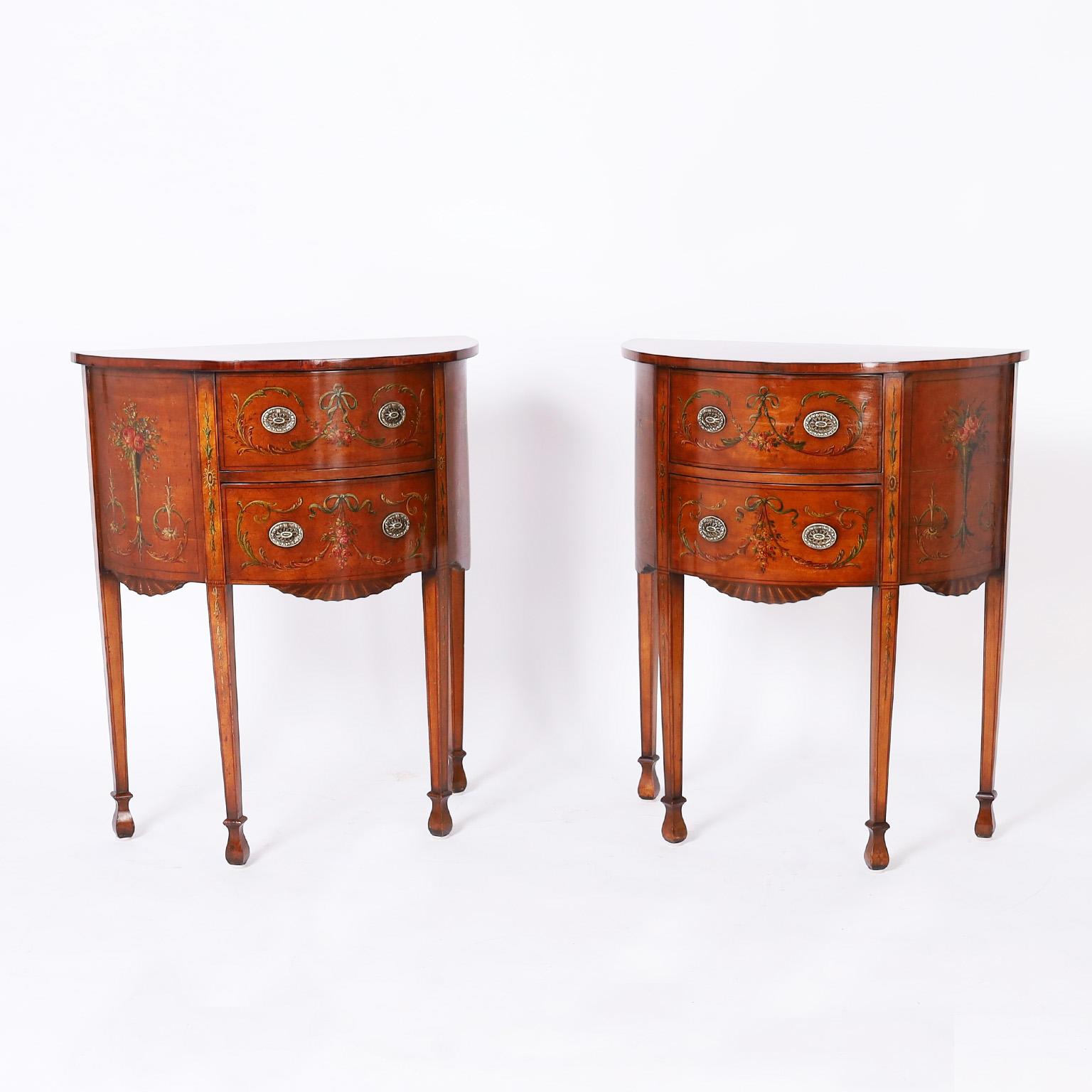 Antique pair of neoclassical stands crafted in mahogany with two drawers in a demi lune form decorated in Adam style romantic floral motifs over a faux crackled finish on long elegant legs. French polished in the traditional old world manner.