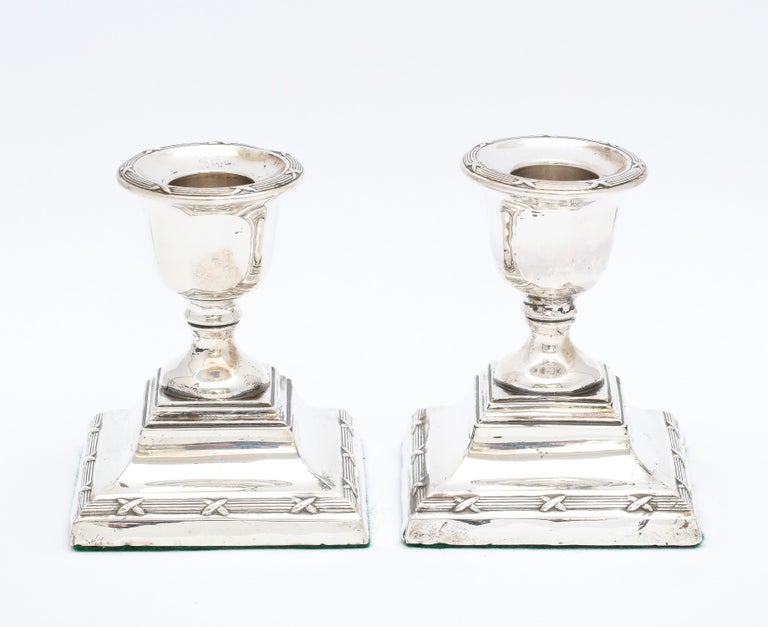 Pair of Edwardian period, sterling silver, Adams-Style candlesticks, each having a ribbon and reed motif on the edge of its candle cup (this ribbon and reed motif is also on the stepped up base of each candlestick), Chester, England, year-hallmarked