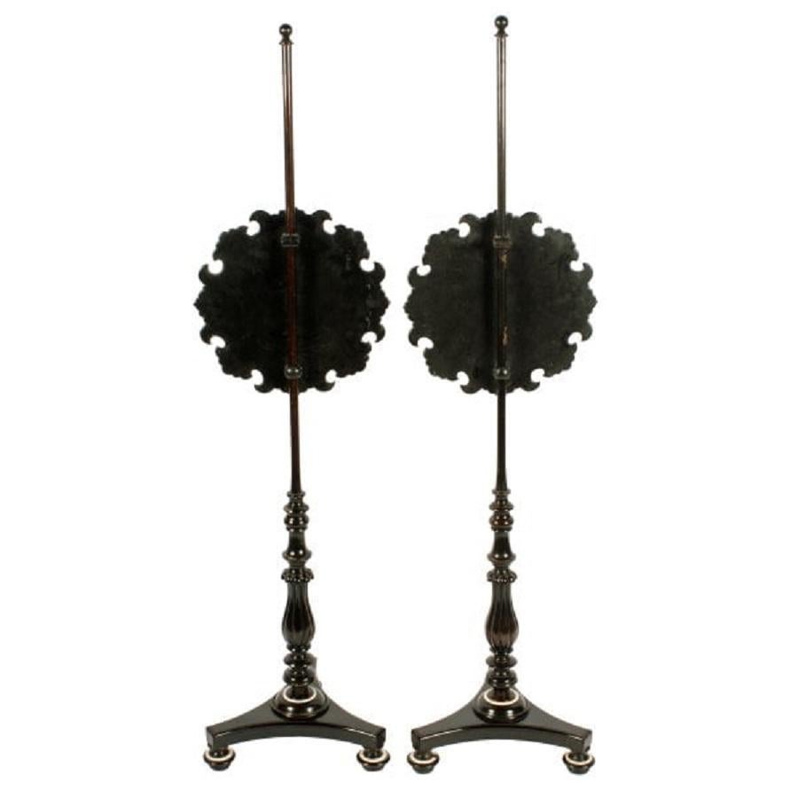 A pair of late 19th to early 20th century pole screens.

The screens are black lacquered and shaped with hand painted scenes of flowers and ribbons.

The poles are ebonised and have triangular bases with bun feet and a reeded baluster shape to