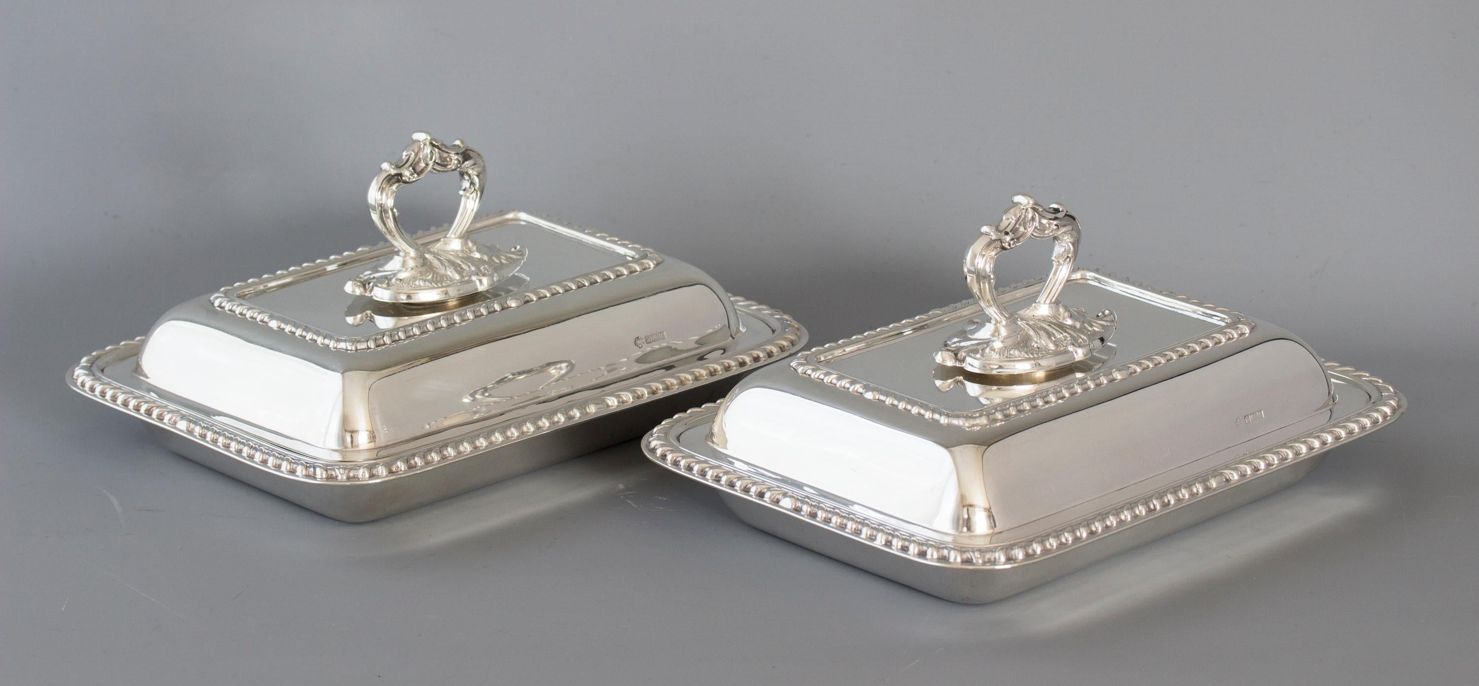 A pair of rectangular silver entree dishes of cushion form with gadrooned edges and ornate cast silver leaf form handles.

Marked for Sheffield 1902 by William Hutton and Sons Ltd. The base, the lid and handle are all marked.

A good pair of