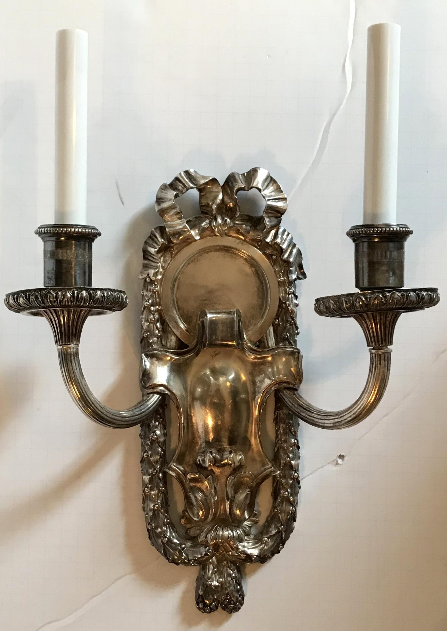 Elegant pair of E.F. Caldwell marked silvered nickel bronze sconces with embellished bow top and framed with filigree draping. With a softly aged gilt bronze patina, the sconces are set off with a wonderful centre medallion, the two fluted arms,