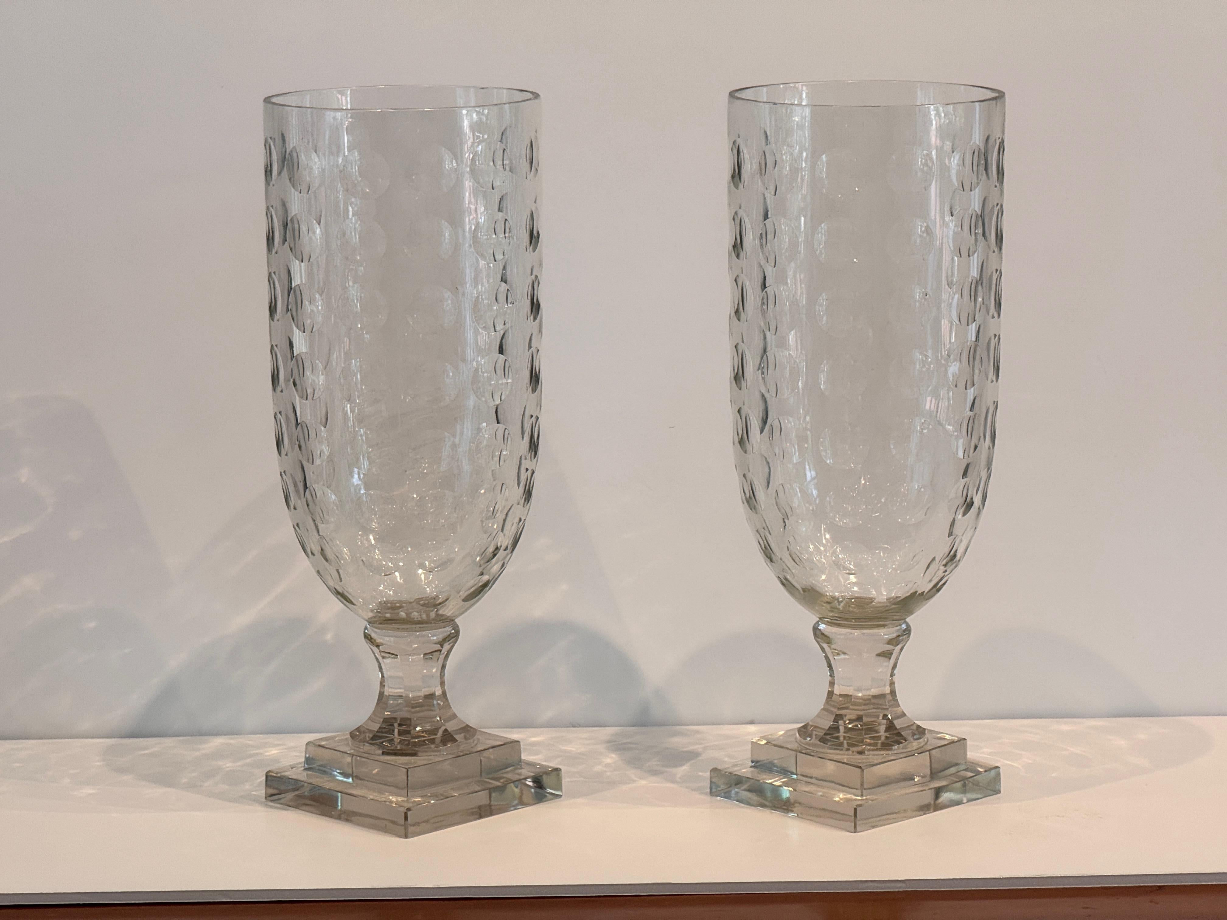 Pair of vintage clear glass urns with an egg-cut surface pattern and stepped square bases. The tall, cylindrical form and raised dot motif give them a modern, decorative presence. Made of clear pressed or cut glass with faceted stems and square