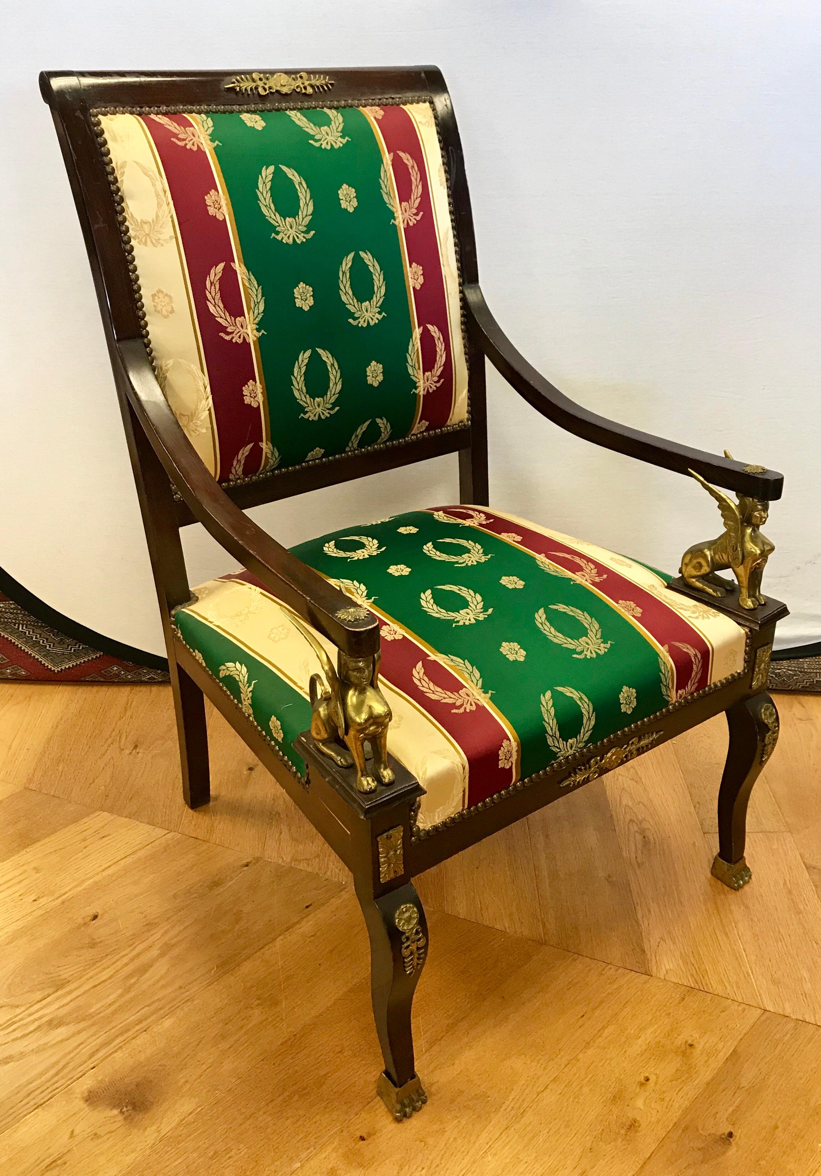 Coveted pair of Egyptian Revival mahogany nailhead arm chairs with gilt bronze mounts. They feature highly decorative Egyptian Revival/Empire touches such as sphinxes, laurels and footings all done in bronze.

They were made in the mid-20th