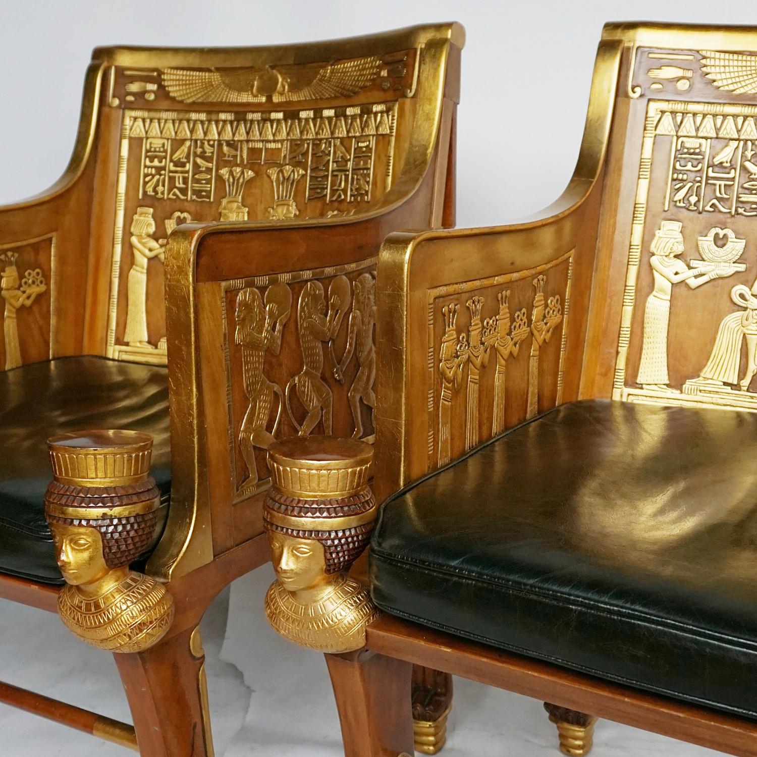 A pair of Egyptian style armchairs. Solid walnut with original gilding. The back is decorated with a winged sun disc, a rectangular panel below depicting a dual image of the seated princess Sitamun receiving a golden collar from the southern