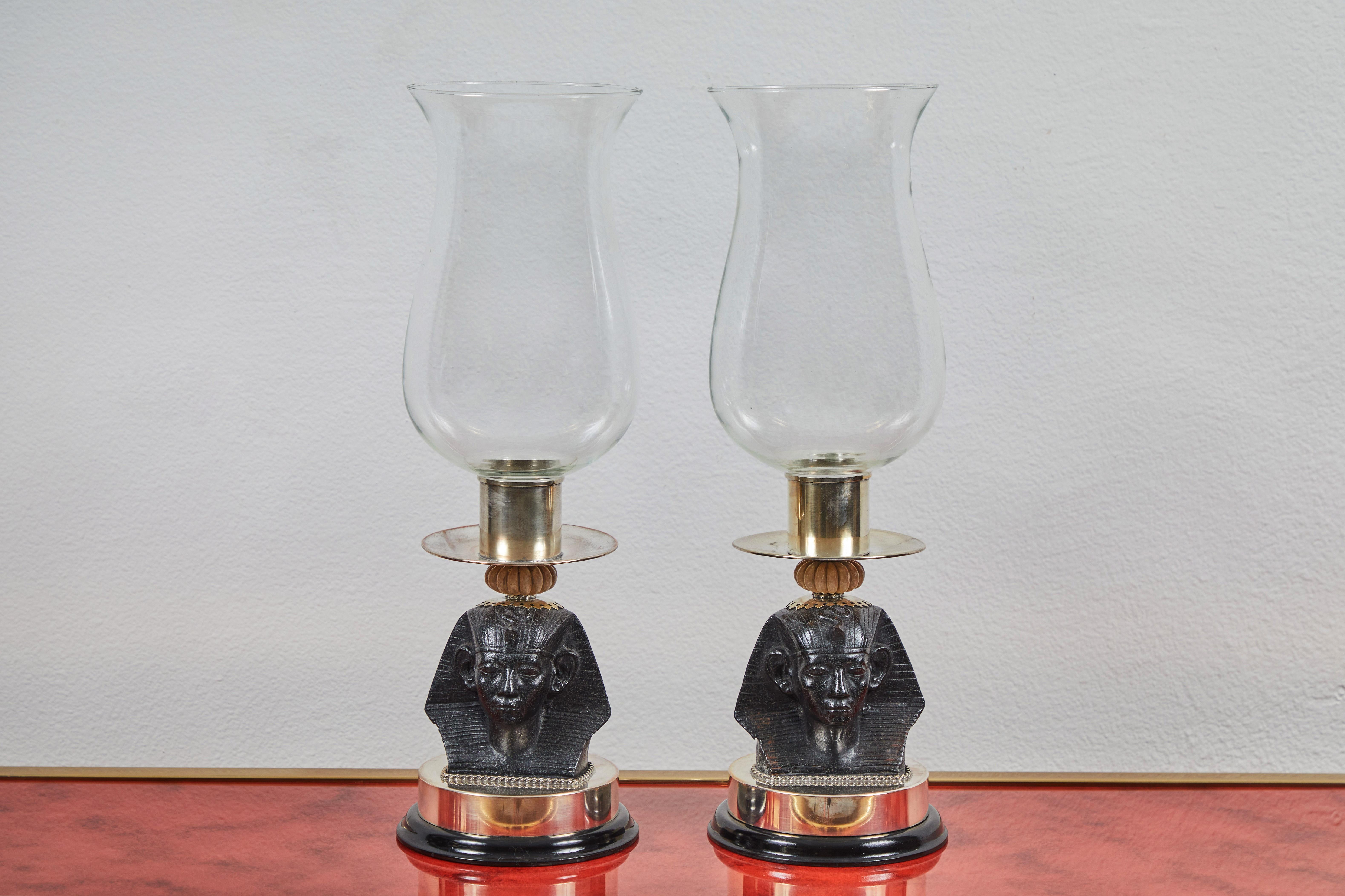 These 1970s candle holders, by Antony Redmile, feature an Egyptian style stone bust and nickel plated brass base. A large glass hurricane sits on top suitable for multiple candle sizes. The plating is in various stages of wear and one pair have