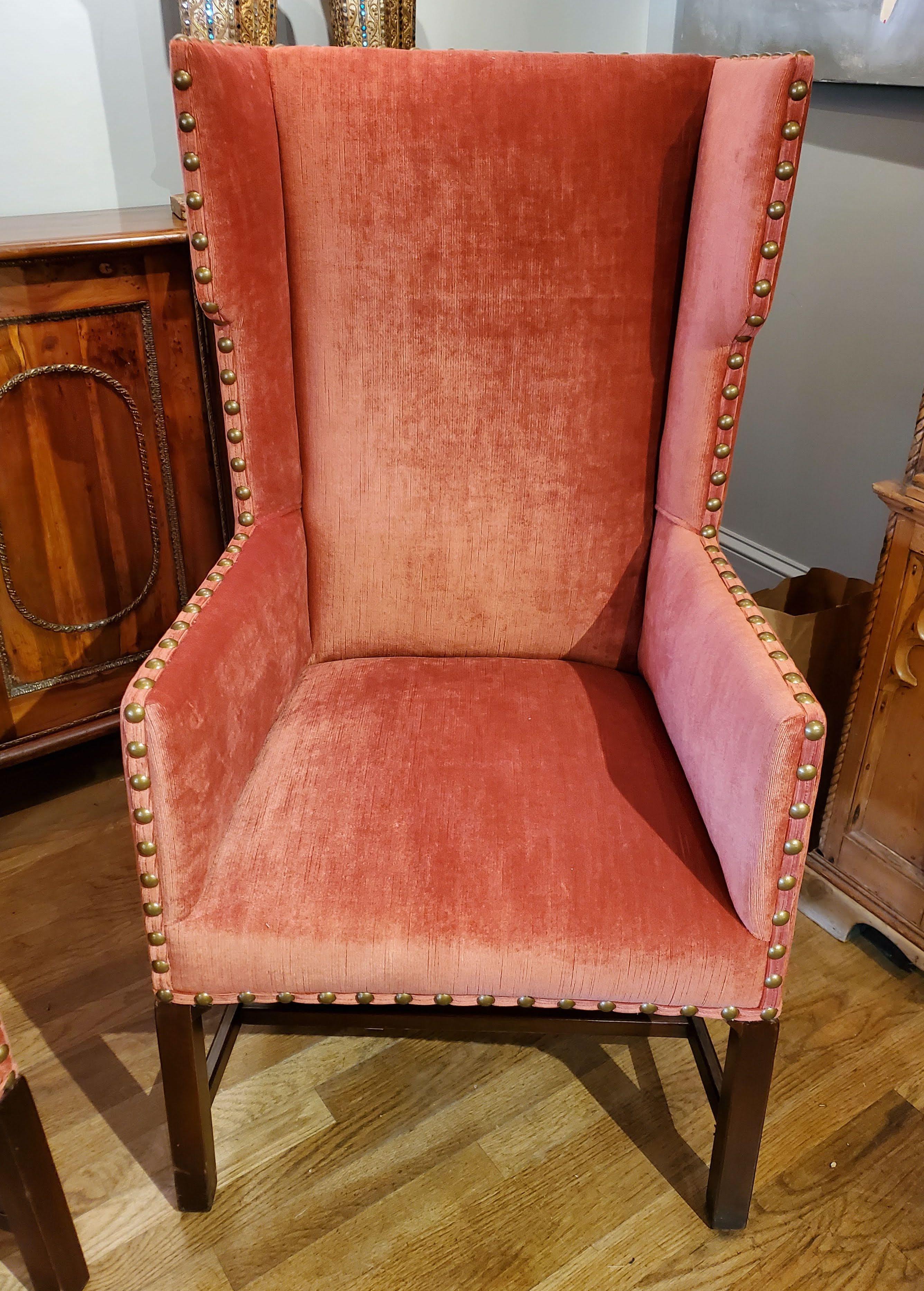 This pair of elegant 19th century English wing chairs are sophisticated, classy and comfortable. Upholstered in persimmon colored velvet with large brass nailhead decoration over mahogany legs and stretchers make for a beautiful addition to your