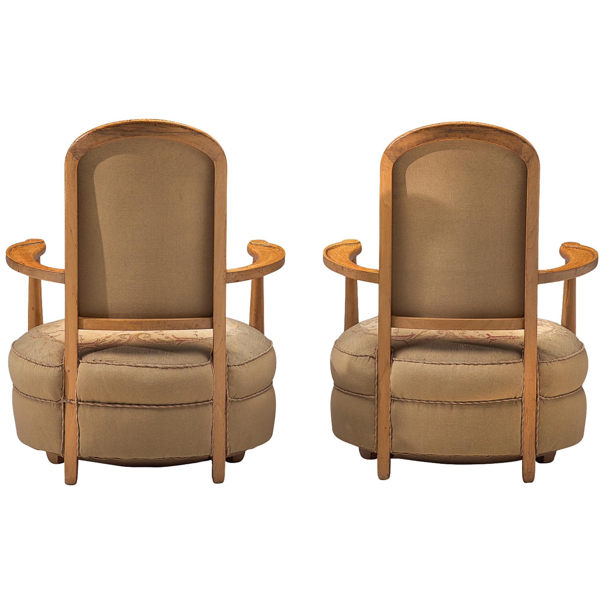 Pair of Art Deco lounge chairs, fabric and oak, France, 1930s.

Exquisite pair of art deco lounge chairs that feature a high majestic backrest. The voluptuous seat is round and the elegant, bended armrests with carved details follow the seat's