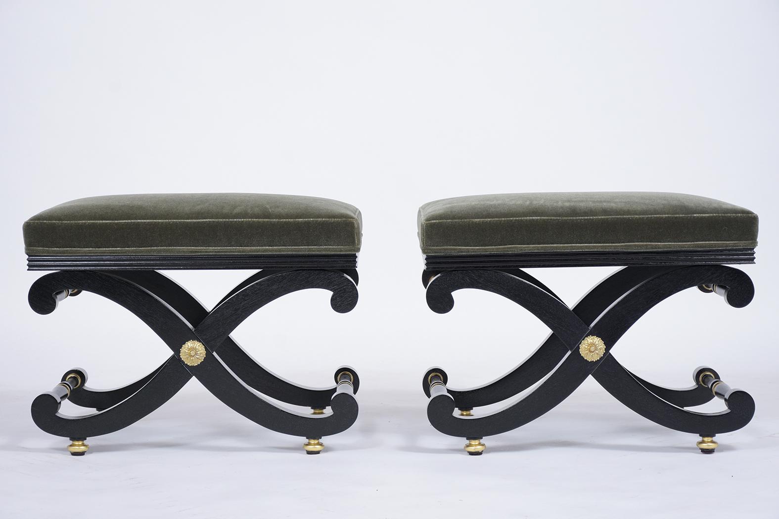 This pair of early 1900s benches have been fully restored, features a sturdy X base frame with brass accents, gilt details, and a newly ebonized lacquered finish. The stools have also been professionally upholstered in a new olive green mohair