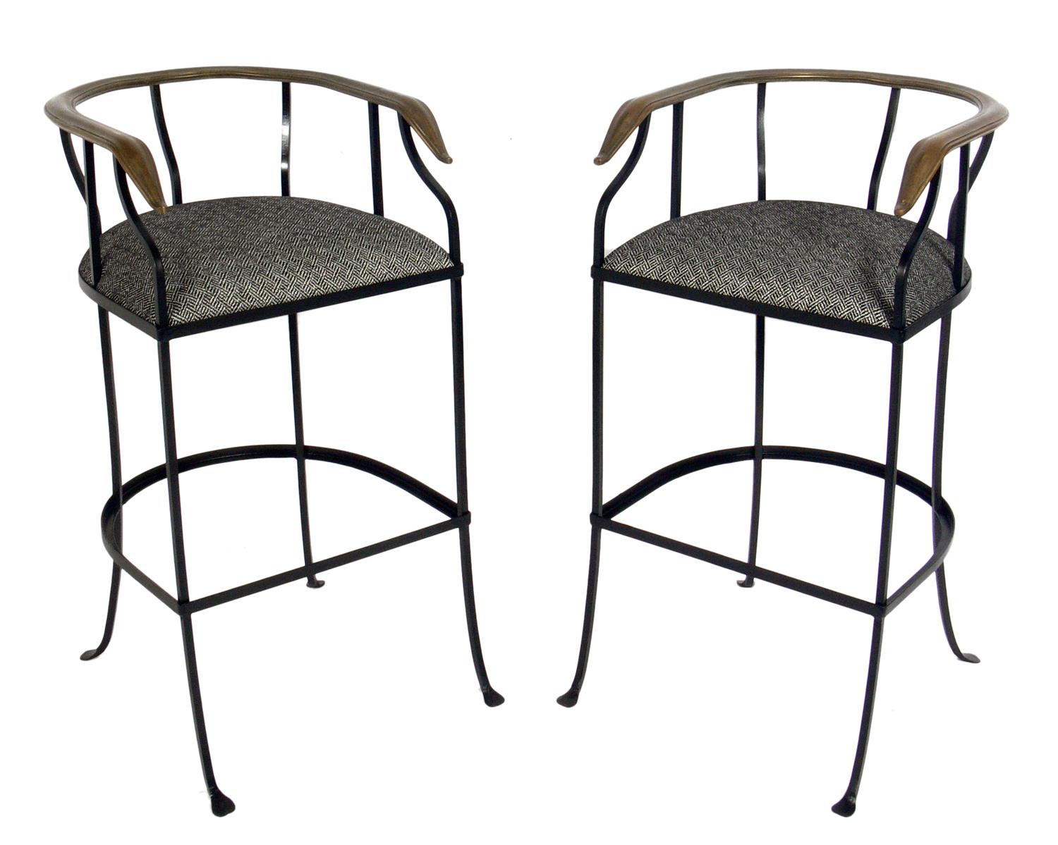 Pair of elegant brass and iron bar stools, American, circa 1950s. They have been beautifully restored with the iron frames painted and new black and white herringbone upholstery installed. The brass horseshoe backrests retain their warm original