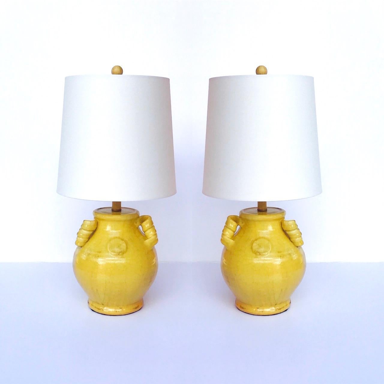 Pair of Chinoiserie Hollywood Regency ceramic urn lamps.  Handcrafted in a beautiful yellow crackle glaze finish with hand painted antiqued patina effect. Lamp features three handles with stylized spirals. Shown with new custom drum shades in white.