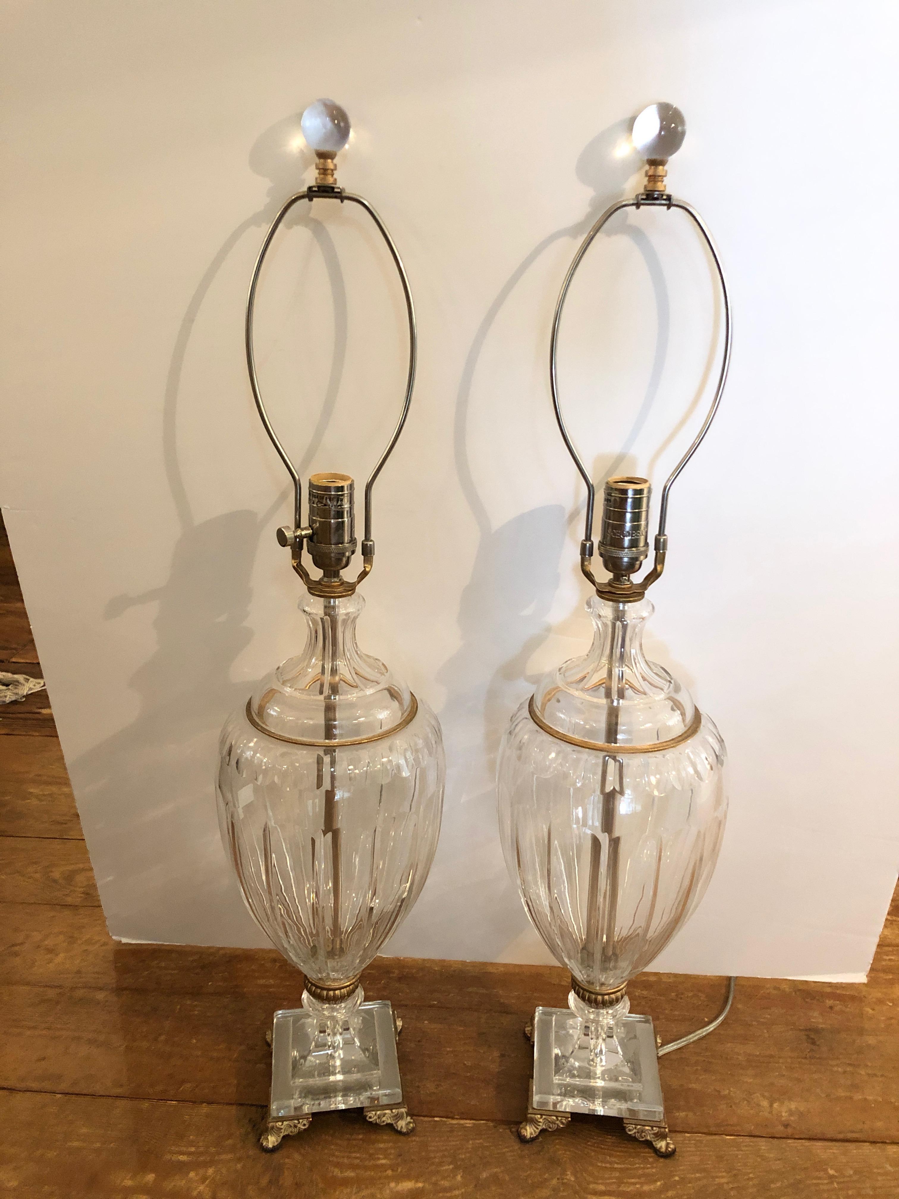Two heavy cut crystal urn shaped table lamps marked Schonbek having pretty brass decorative embellishments and feet as well as lovely custom silk shades. Clear glass ball finials.
Urns are 19 H.