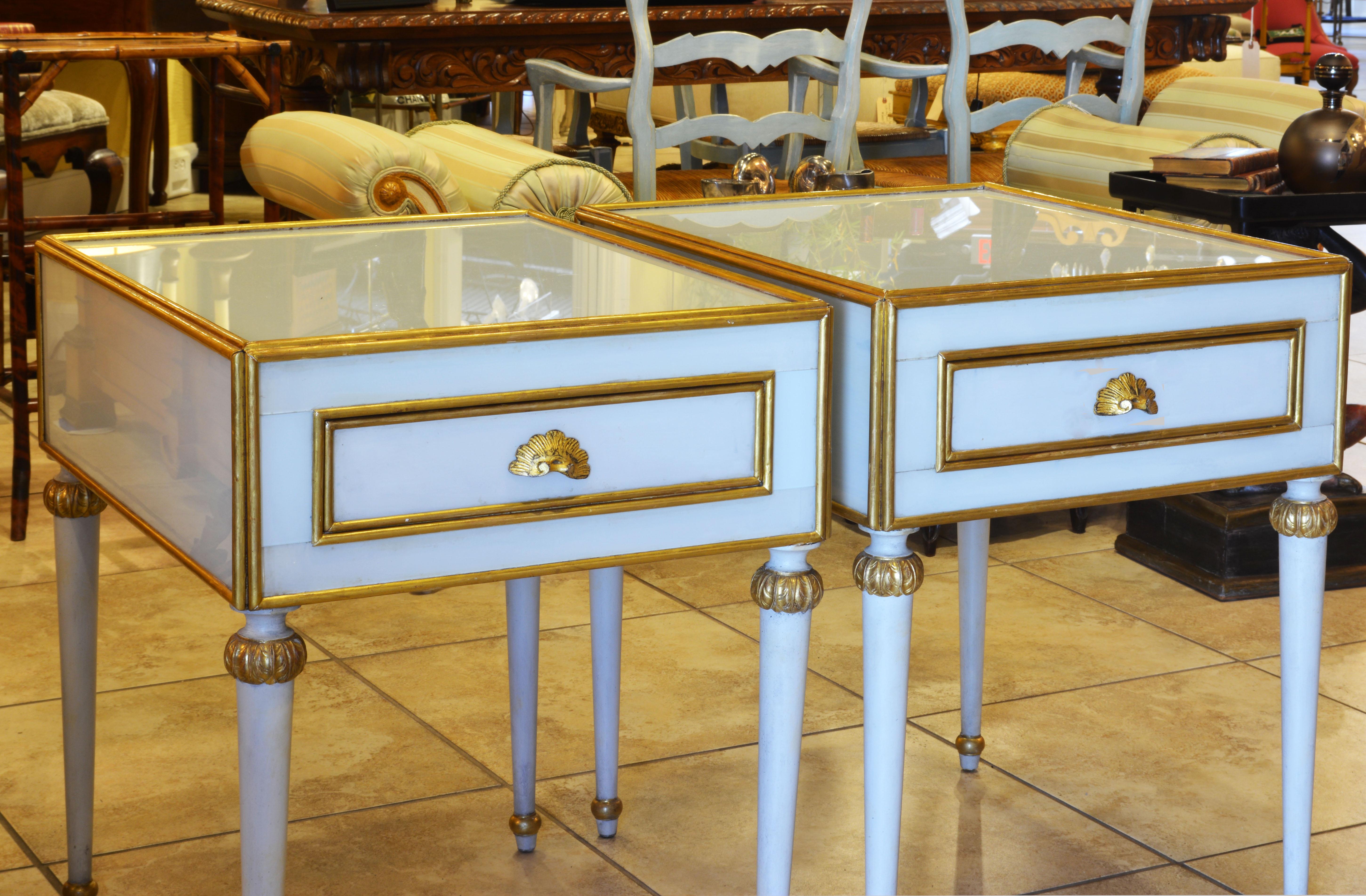 This unusual pair of French Louis XVI style milk glass mounted one drawer side tables feature bodies mounted with giltwood edged milk glass on top and sides resting on four round tapering legs with giltwood accents. The likely date to the