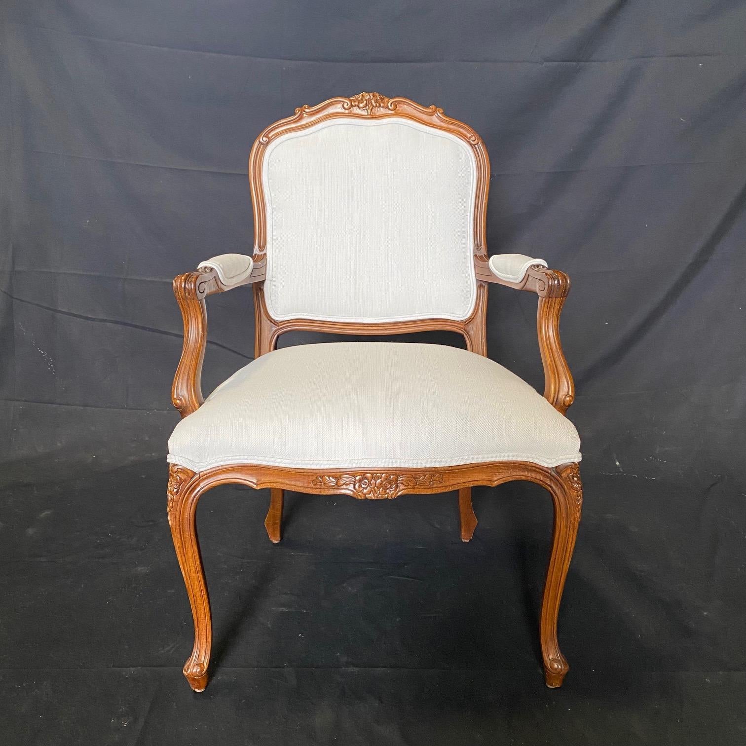 Pair of French Louis XV style walnut carved open armchairs with a lovely shaped back and newly upholstered seat, arms and backs. Can also be used as end accent dining chairs or in a bedroom or sitting area. Will add elegance to any room.  arm height
