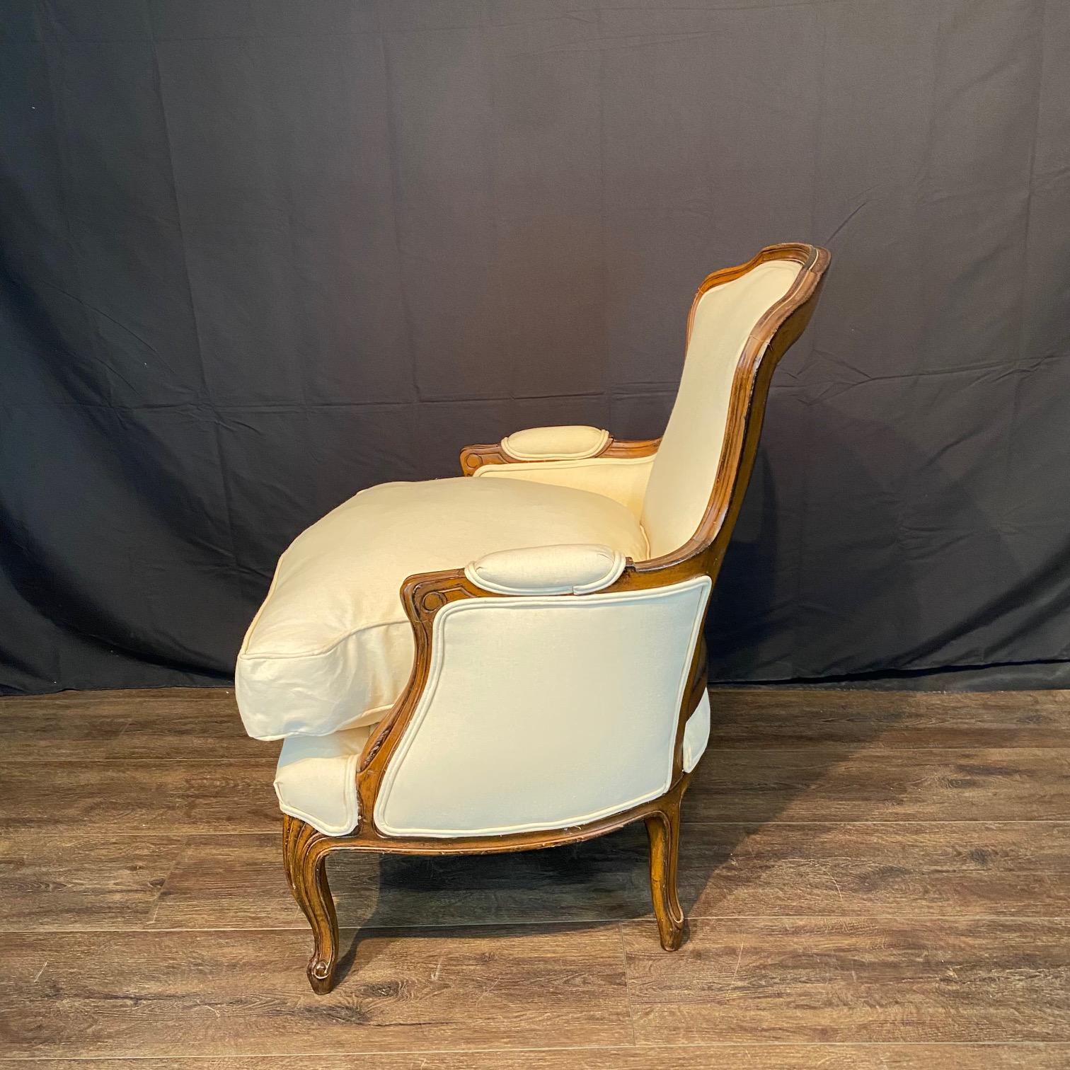 Elegante coppia di sedie o poltrone bergere francesi Luigi XV in noce intagliato del XIX secolo, recentemente rivestite in tessuto di cotone lino bianco sporco. Dettagli intagliati con gambe a cabriola graziosamente affusolate che terminano con