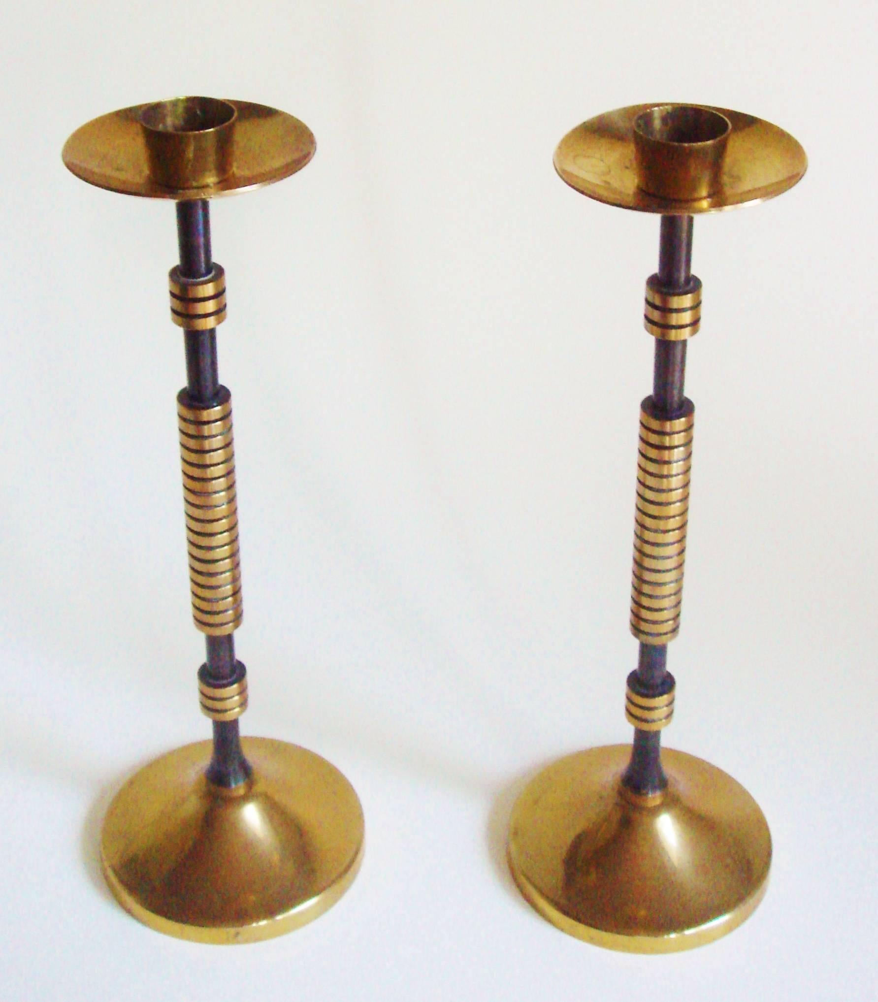 This pair of very elegant and slender French Art Deco or Machine Age brass and black candlesticks feature a black enameled central rod. This rises up from a bell-shaped circular base and culminates in a brass dish-shaped bobeche beneath a brass