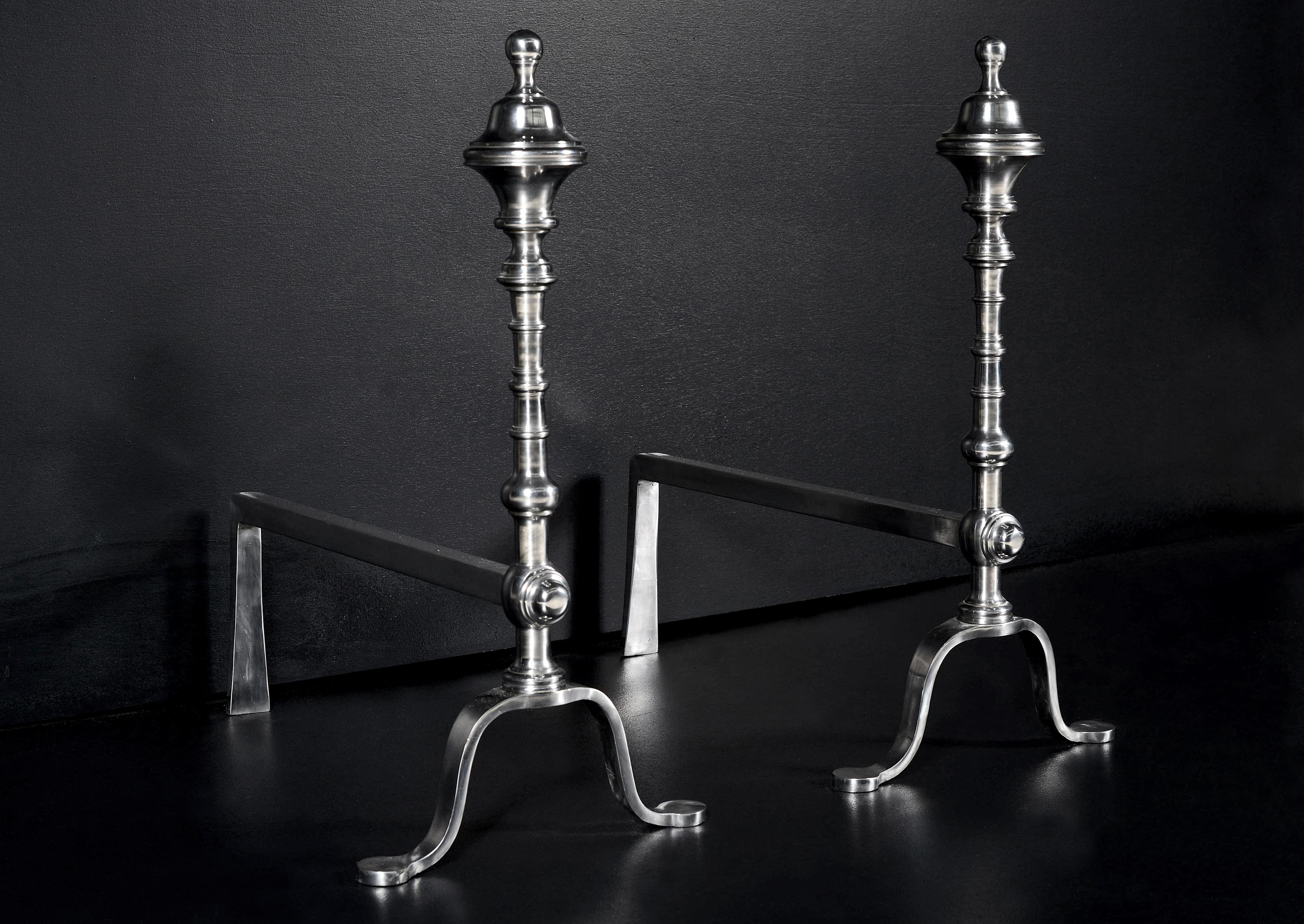A pair of good quality elegant Georgian style English steel firedogs. The turned uprights surmounted by urn finials. Pictured with polished back bar which could be blacked if required.

Measures: 
Height:	590 mm      	23 1/4 in
Width:	300 mm     