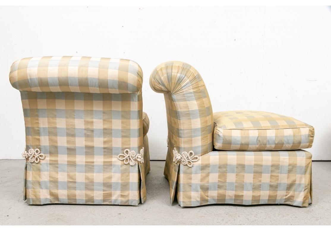 The Slipper Chairs in an ample size with sloping scrolled backs, the seats with deep tailored skirts. Upholstered in a fine taffeta type fabric in ecru, tan and pale blue plaid. With fine ecru braid frogs decorative attachments at the junction of