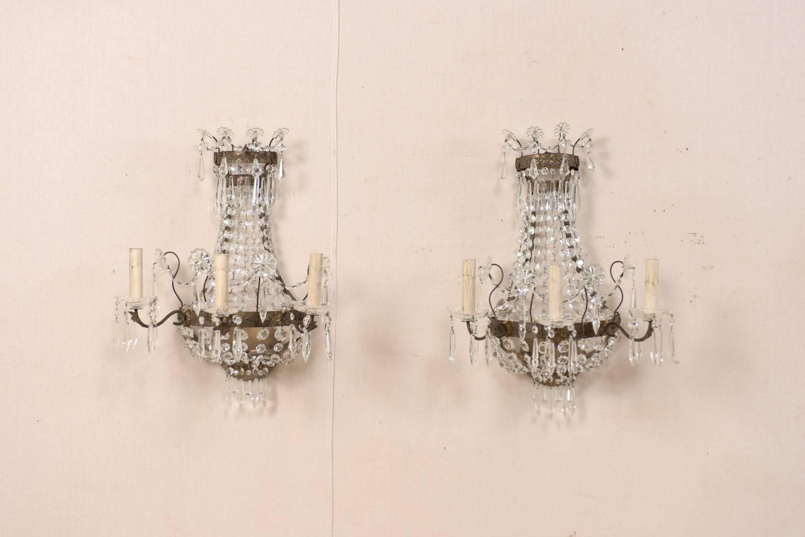 A pair of Swedish three-light crystal and cut-glass wall sconces from the mid-20th century. This pair of vintage wall candelabras from Sweden each feature a frame of patinated bronze, an upper crown adorned with glass-cut flowers and crystals,