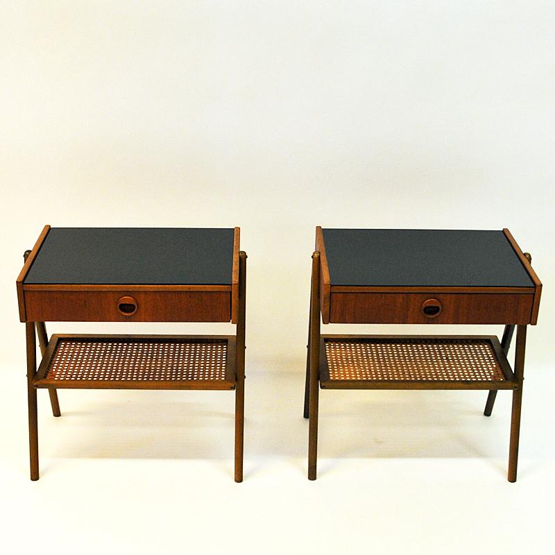 Nice and elegant pair of teak and glass top bedside tables with drawers and four slightly tilted legs. The night table tops has black painted shiny glass plates on the surface. Underneath a rotting shelf for newspaper, books etc. Scandinavia, circa