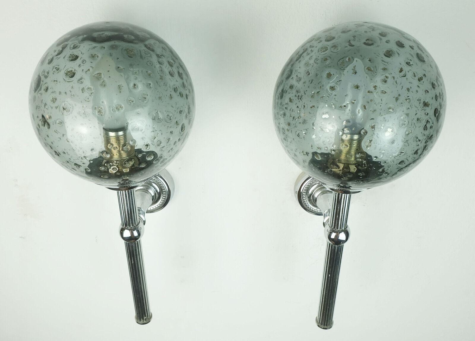A beautiful and elegant pair of sconces manufactured in the 1960s to 1970s. The base is made of chrome-plated metal with a slight art deco touch in the design. The ball-shaped shades are made of blueish gray smoked glass with slightly metallic