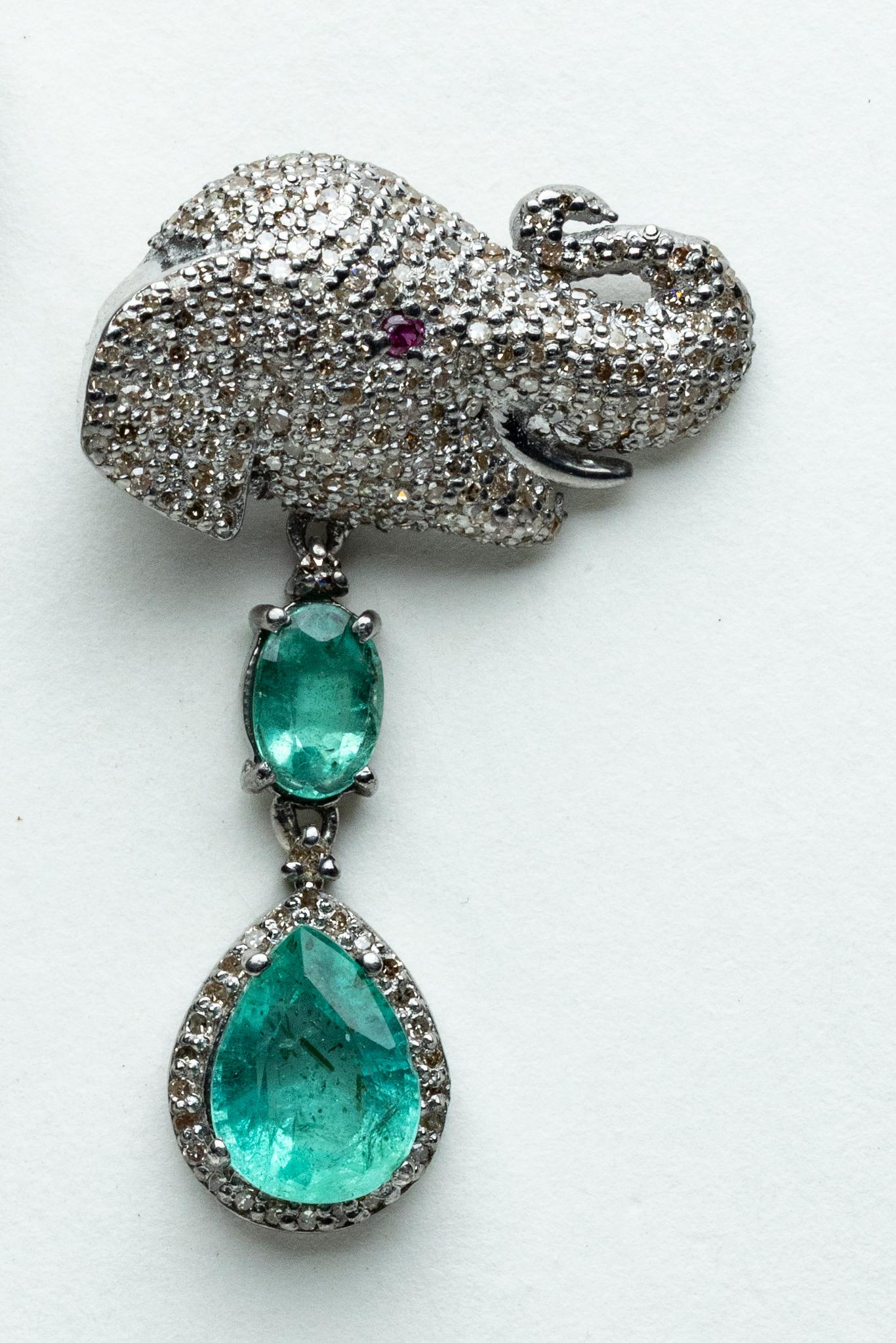 Pair of unusual elephant motif dangle earrings featuring pave`-set, round brilliant cut diamonds and ruby eyes on the elephant head post.  Dangling from the post are oval, faceted emeralds and a pear-shaped emerald bordered with pave`-set diamonds. 