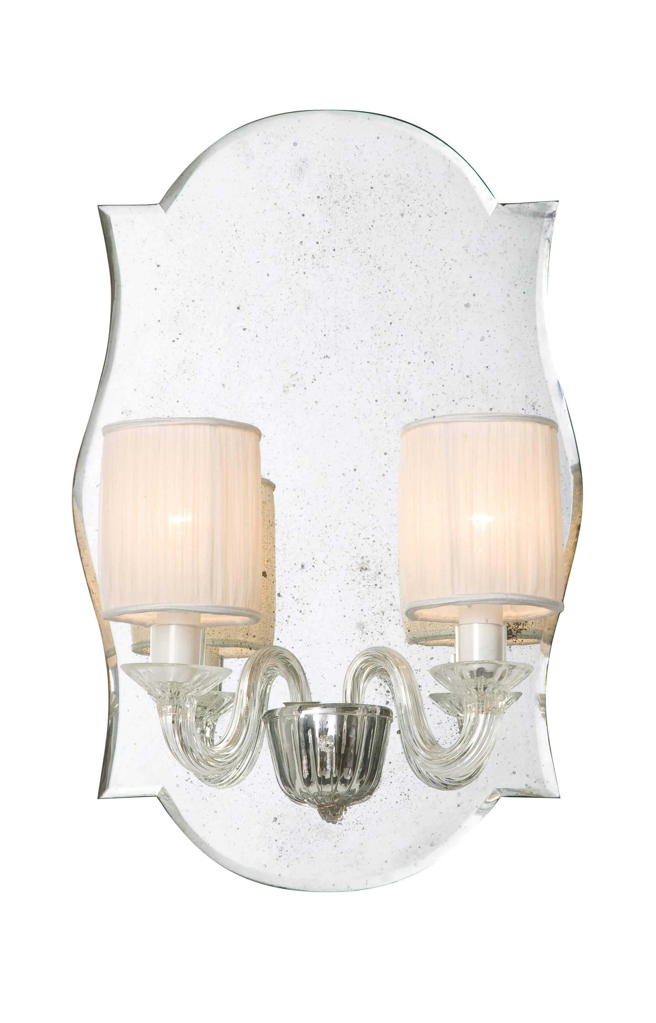 Hand blown Murano glass wall lights with straight ribbing finish in clear glass and fitted on an antique finish bevelled mirror. One pair only.
Two E14 bulb fittings.

Note: Pleated cream shades will be supplied with these wall lights. These are