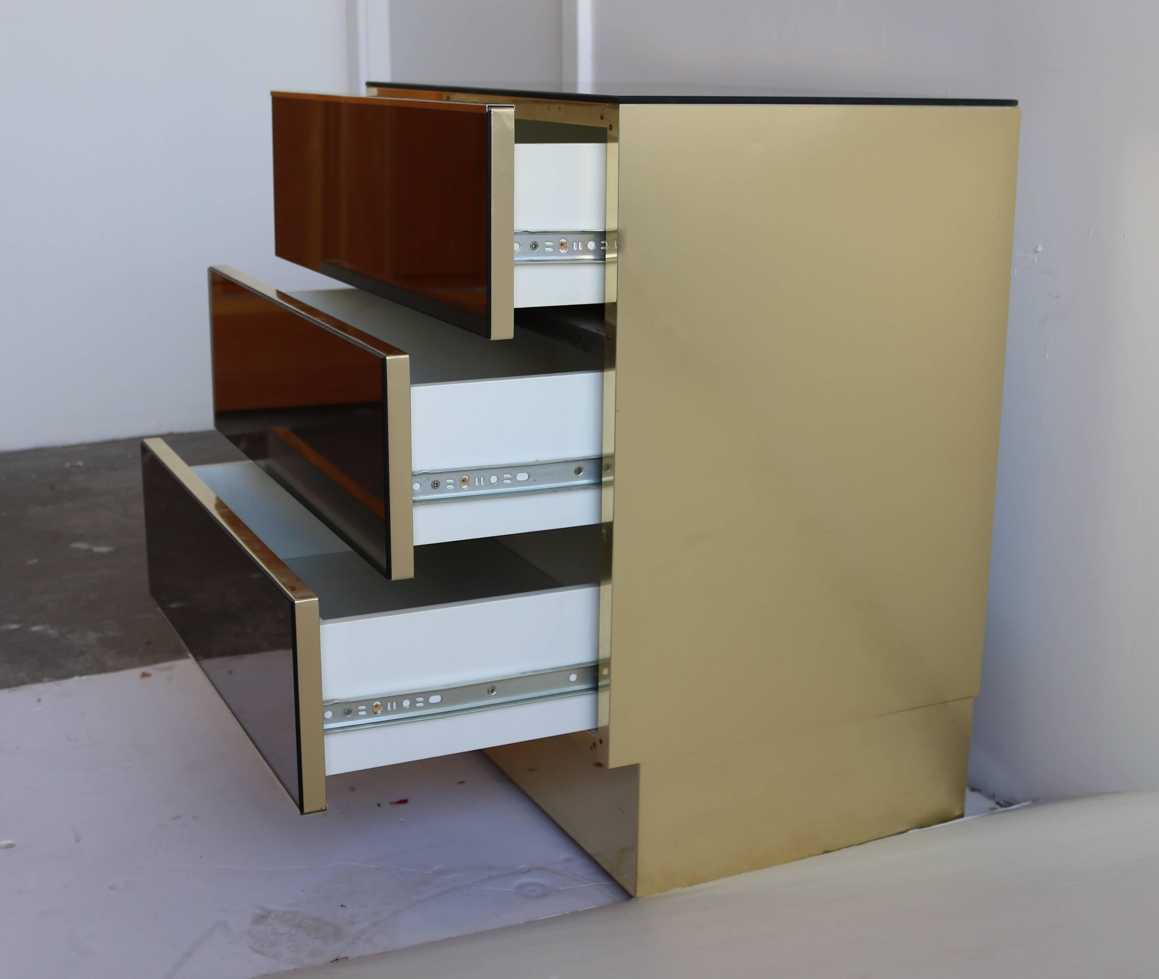 Beautiful pair of vintage Ello three-drawer nightstands, circa early 1970s. These rectangular stands havesmoked mirror face drawers and top, and brass paneled sides.